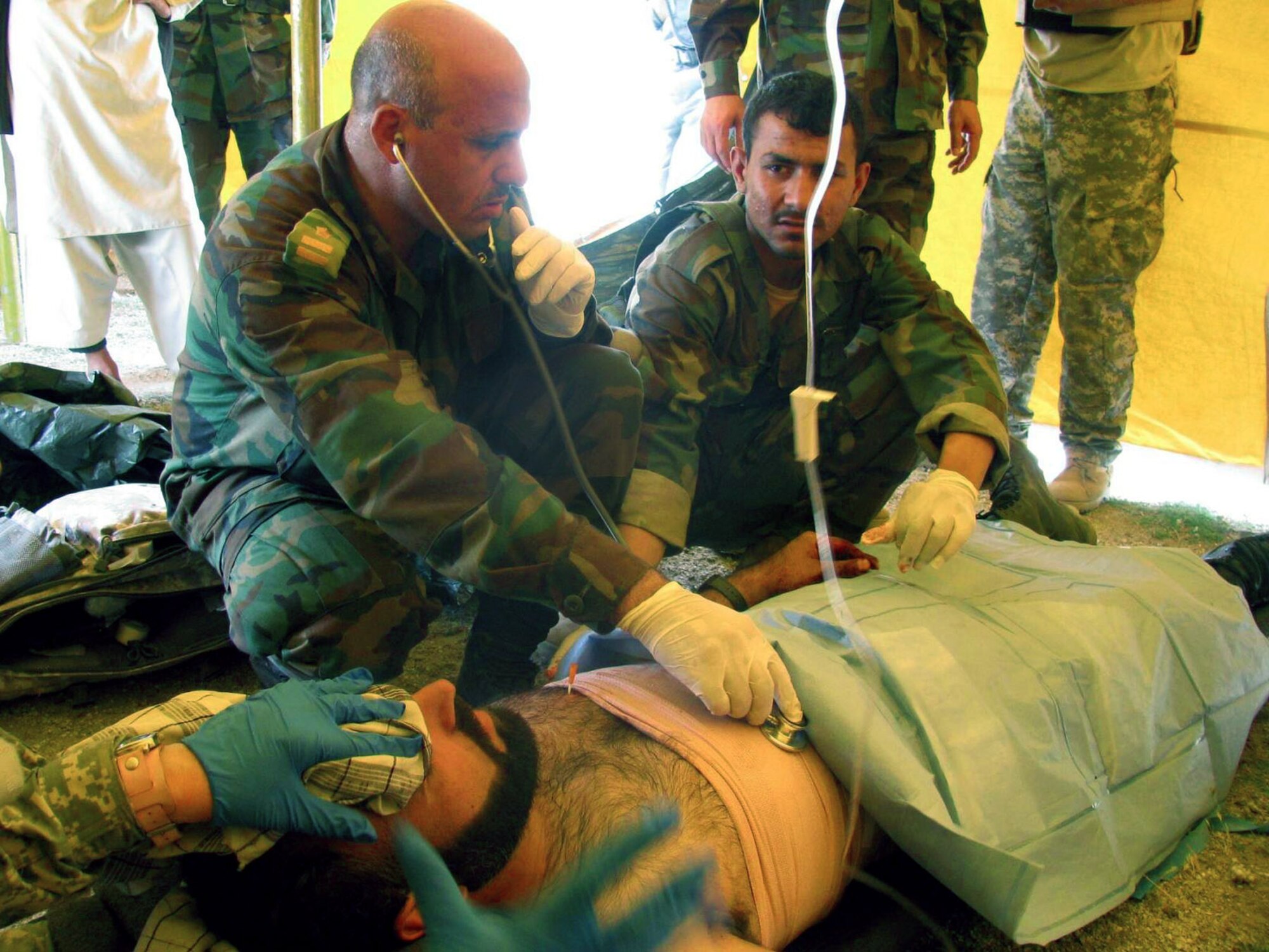 Dr. Mohammad Yasuf treats a wounded Afghan national police officer successfully stabilizing him after the officer received a gunshot wound May 7 in the Laghman Province in Afghanistan. Dr. Yasuf, an Afghan national army doctor, and Laghman Provincial Reconstruction Team medics were engaged in a joint-medical outreach in the Sangar Valley at the time. The Afghan national police were conducting an unrelated poppy-eradication mission a few kilometers away when the officer was wounded. (U.S. Air Force photo) 
