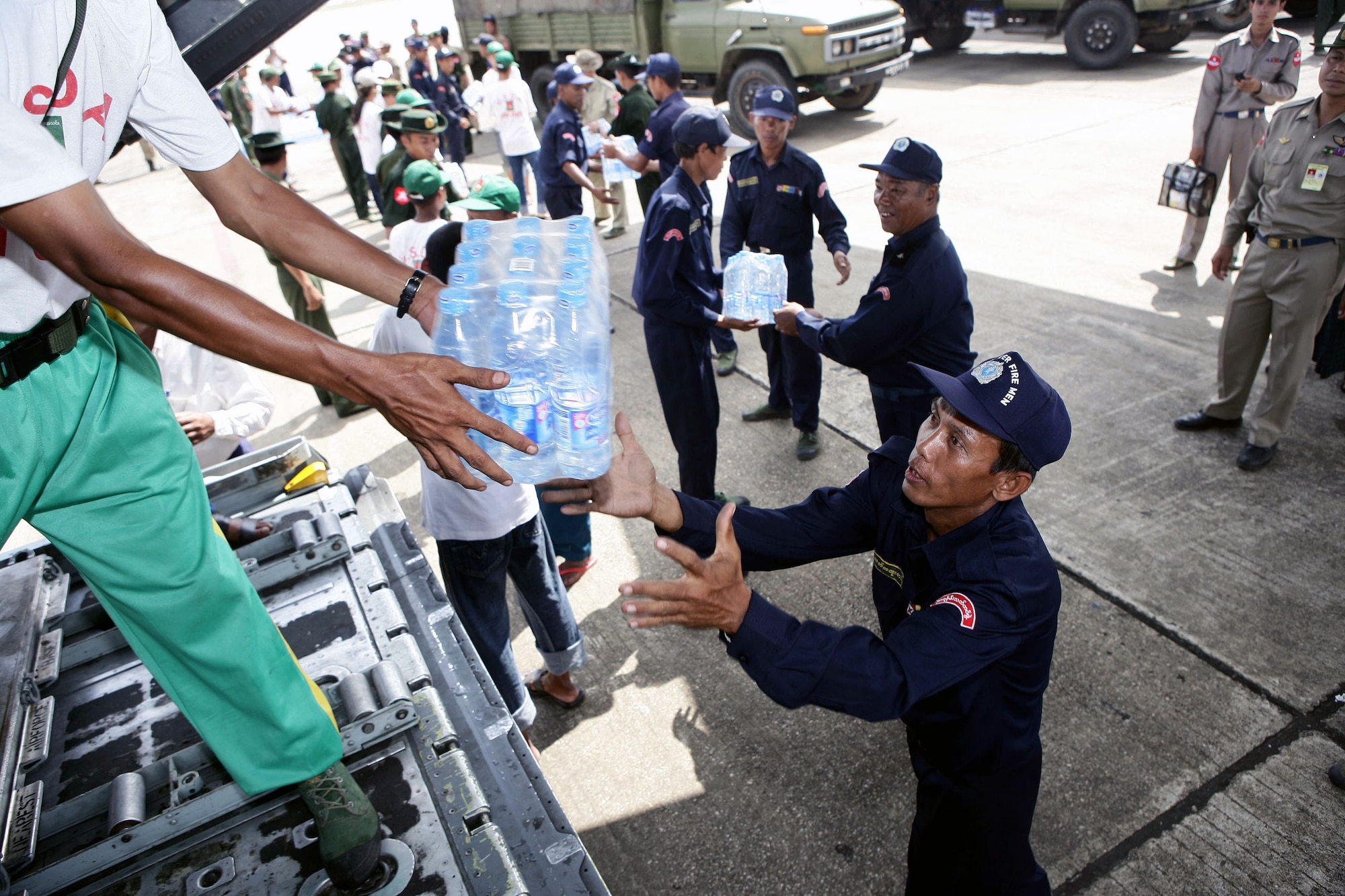 A civilian aid worker from Burma hands bottled water to a Burma servicemember from a U.S. Air Force C-130 Hercules May 12 at the Yangon International Airport in Burma. The plane carrying water, food and medical supplies provided relief to Burma, which was struck by Cyclone Nargis May 2. (U.S. Marine Corps photo/Sgt. Andres Alcaraz) 
