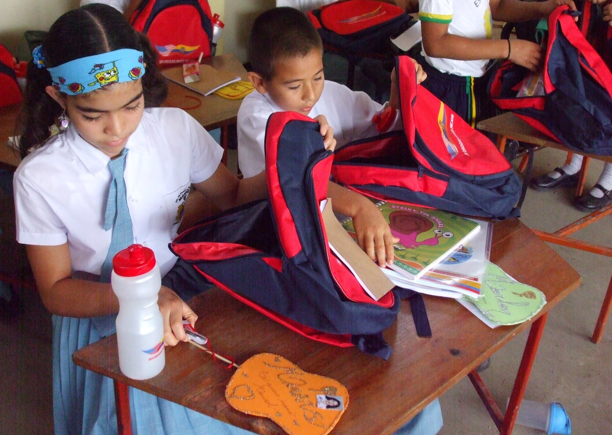 Children at the school, Xxxxxxxx Xxxxxxxxx in the town of Xxxxxx look through the contents of their new backpacks DAY OF WEEK.  Last week members of FOL Manta helped give away 6,500 backpacks to underprivileged children in Manabi province.  Each student received a backpack embroidered with the Spanish phrase, without drugs you live better, and inside each backpack was a water bottle, paper, pencils and children in grades 3-6 received a Spanish-English dictionary.  (U.S. Air Force photo/Chaplain (Capt.) Steven Survance)