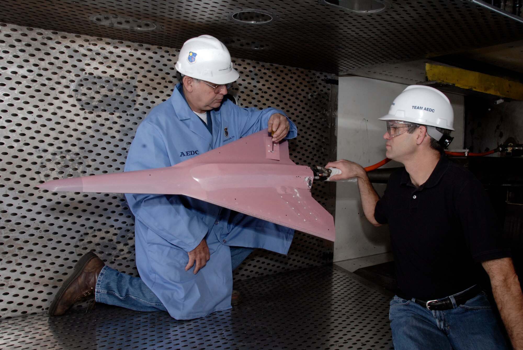 From left, Dennis Odear, Aerospace Testing Alliance outside machinist at Arnold Engineering Development Center, Arnold Air Force Base, Tenn., makes an adjustment to the tailless aircraft model in the four-foot transonic wind tunnel while Brant Maines, the Lockheed Martin Corp. program manager on the test, watches. (Photo by Rick Goodfriend)