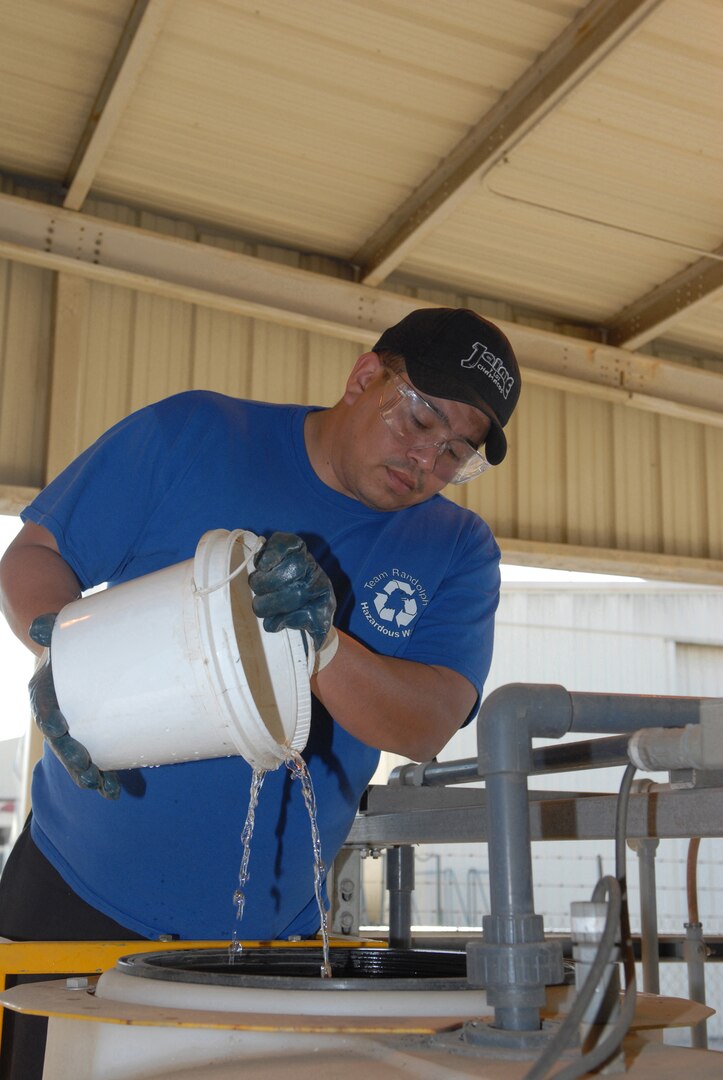 Harmin Aguilera, a contractor working for the 12th Civil Engineer Division, pours acid into a holding tank in preparation to dispose of the acid as hazardous April 29. (U S Air Force photo by Don Lindsey)