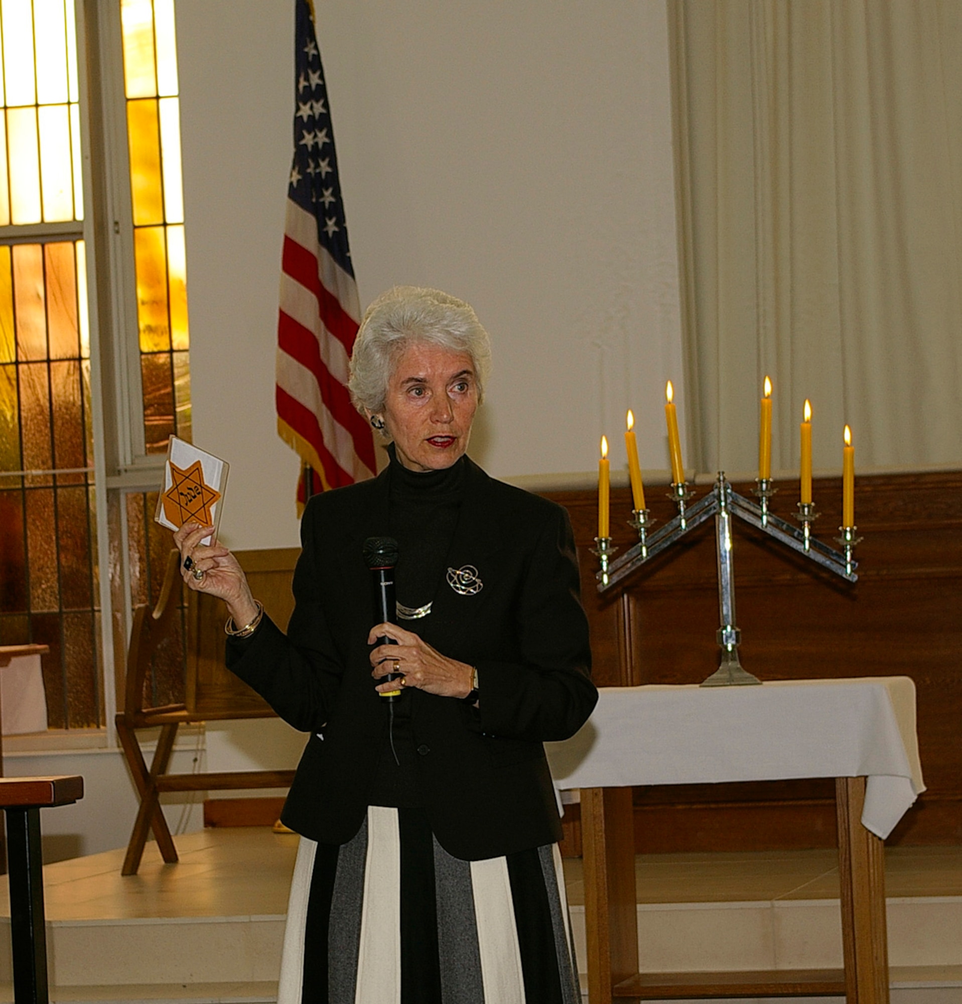 Eva Clarke, shows a yellow star, given to her by a Holocaust survivor, to those attending the Holocaust Remembrance ceremony May 2 at the RAF Mildenhall Chapel. Born during the Holocaust, three days before the U.S. Army liberated the concentration camps where her Jewish parents were prisoners, Eva shared her mother's story of three years in German prisoner-of-war camps during World War II. Her mother was Czech and her father was German; both were Jewish. (U.S. Air Force photo by Karen Abeyasekere)