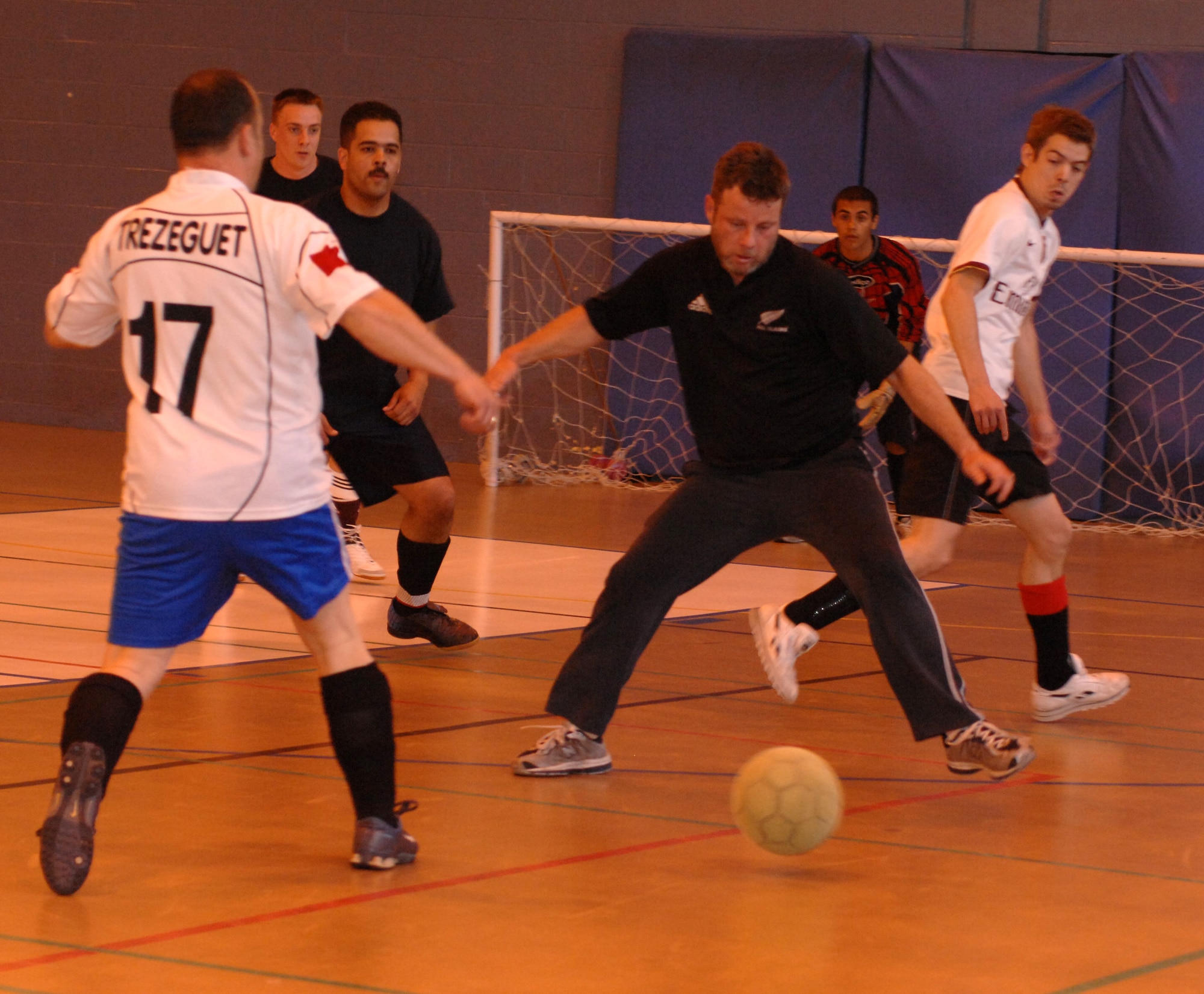 Shane Hall, (track pants, black shirt) 100th ARW/JA , tries to block the ball from 100th CES player John Cooper (17), in the indoor soccer championships at the Northside Gym, May 8. (U.S. Air Force photo by Airman 1st Class Brad Smith)