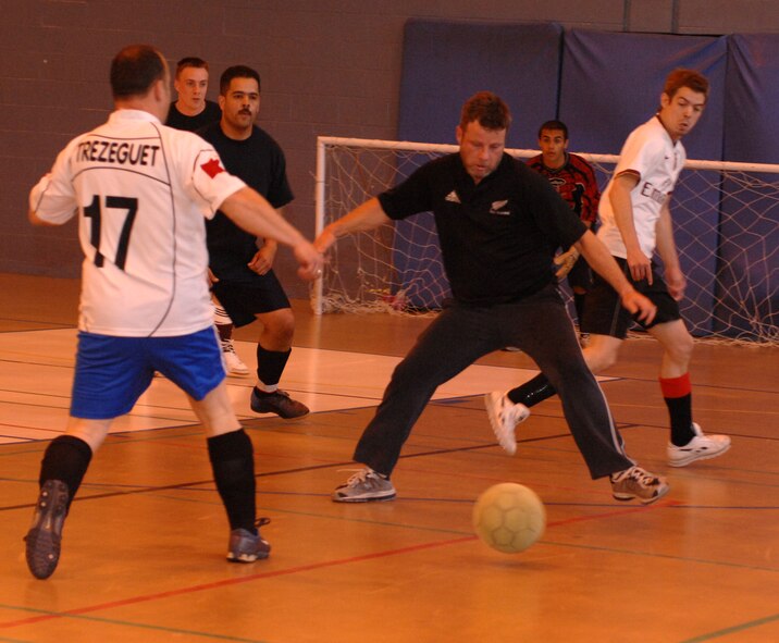 Shane Hall, (track pants, black shirt) 100th ARW/JA , tries to block the ball from 100th CES player John Cooper (17), in the indoor soccer championships at the Northside Gym, May 8. (U.S. Air Force photo by Airman 1st Class Brad Smith)