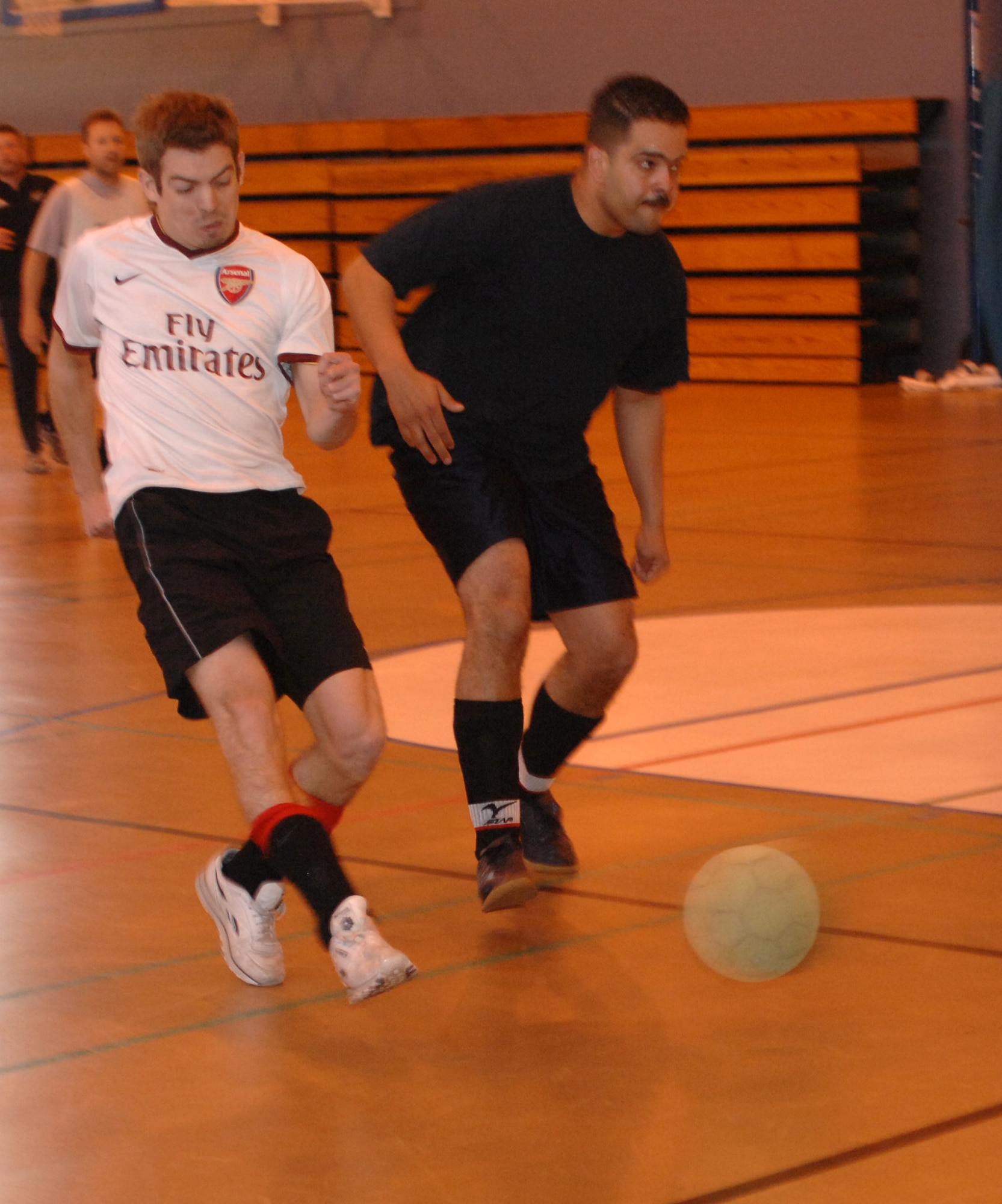 Geoff Gough (white shirt), 100th CES player, goes around Ivan Swarz from 100th ARW/JA and shoots on goal. Gough scored the first goal in the indoor soccer championship at the Northside Gym, May 8. (U.S. Air Force photo by Airman 1st Class Brad Smith)