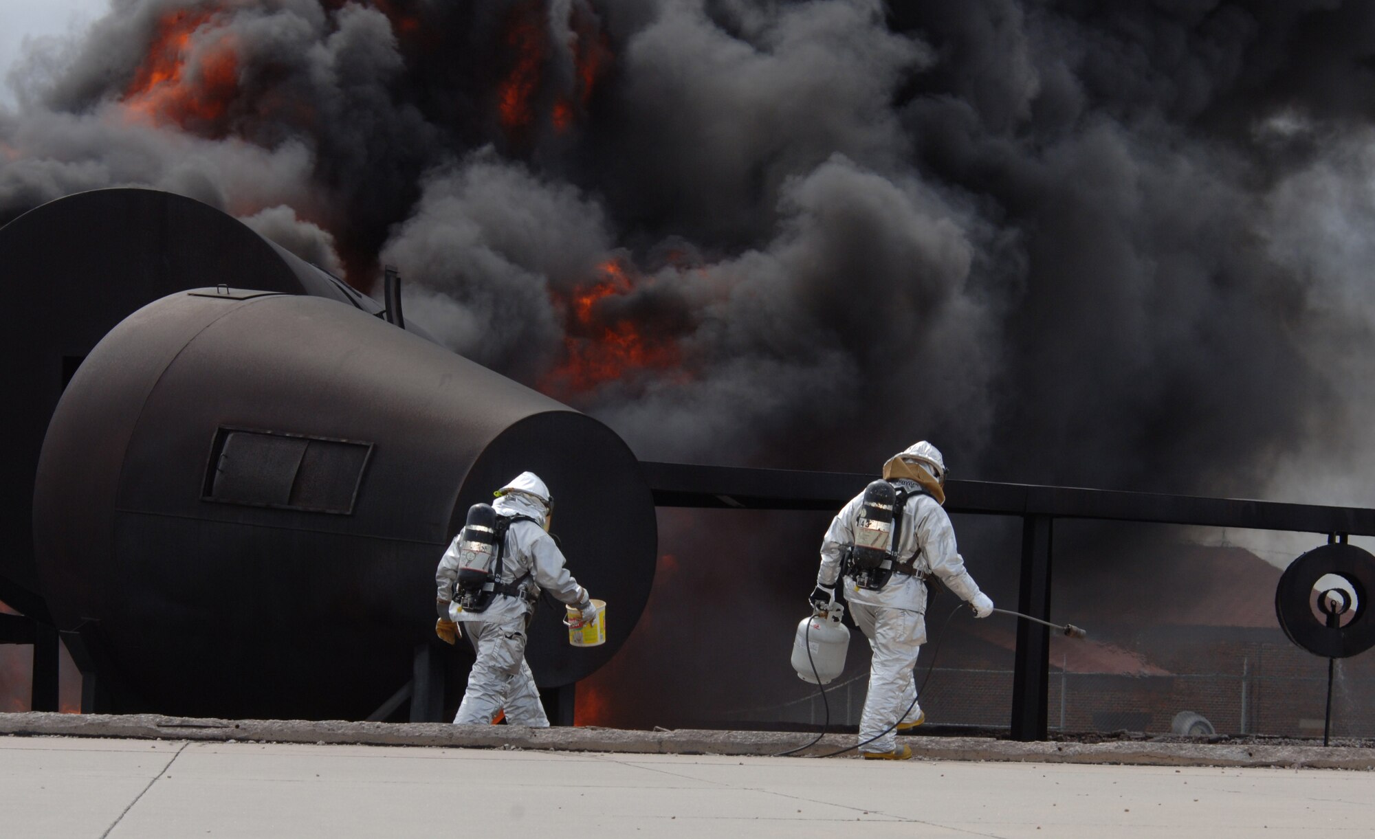(Right) Staff Sgt. Kristian Voth, 114th Air National Guard Civil Engineer Squadron fire fighter crew chief, ignites flames with a propane lighter as Staff Sgt. Ray Granillo 28th Civil Engineer Squadron drops flammable liquid to intensify the training pit fires at Ellsworth, May 13. Ellsworth Airmen and South Dakota Air National Guard members worked together to earn their annual Airport Fire Fighter Certification and to improve their fire fighting skills.  (U.S. Air Force photo/Airman Corey Hook)