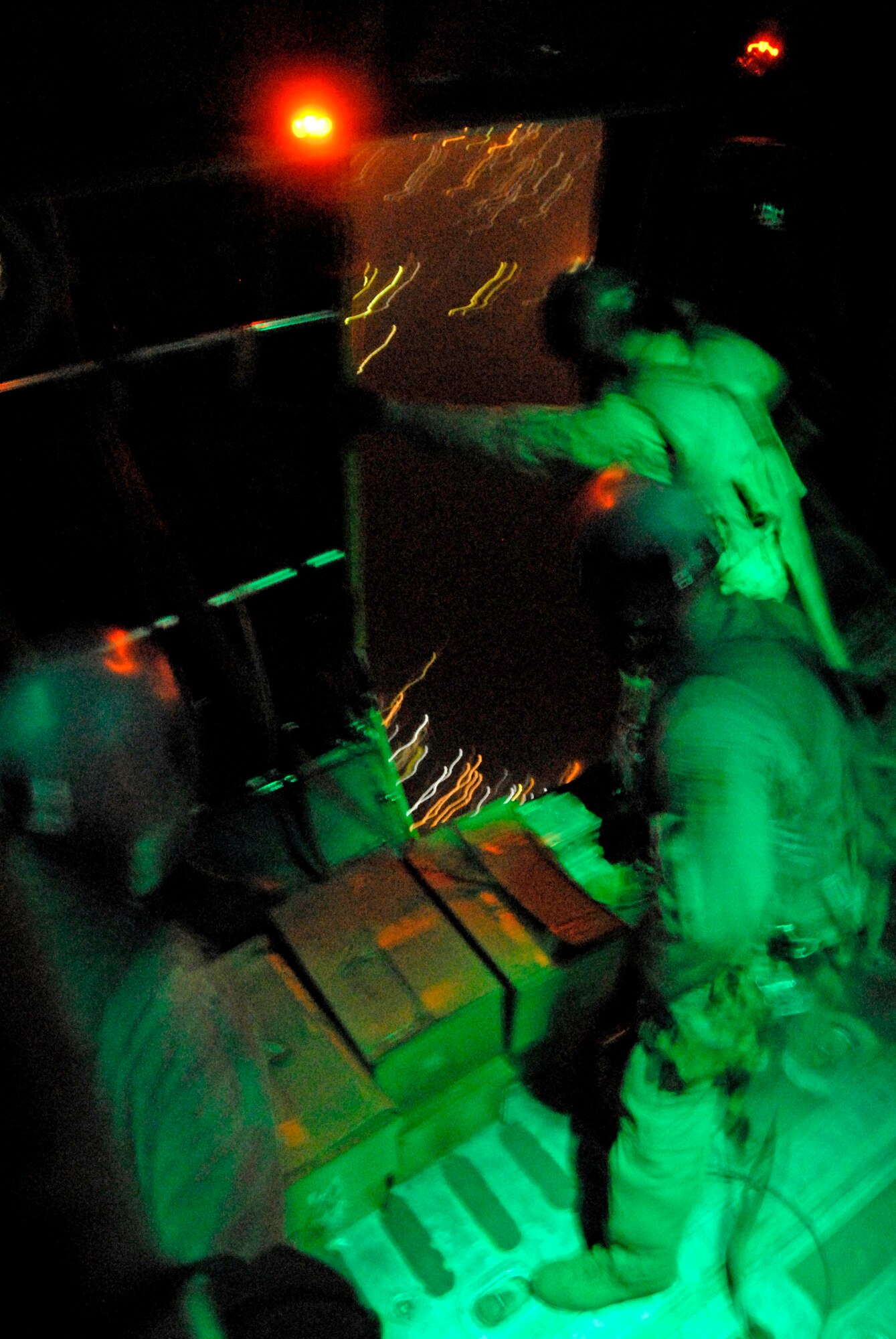 Aircrew members from the 737th Expeditionary Airlift Squadron wait for the light above the right rear troop door to turn green before they push out several hundred thousand leaflets over an Iraqi city recently. The three-person team includes 1st Lt. Justin Fitzpatrick (left) and Senior Airman Joel Pfaff (center), who fill the roles as feeders to Staff Sgt. Gabriel Molanders (right), the kicker on the team who ensures the leaflets get out the door and over the target area. All three aircrew members are deployed from Dyess Air Force Base, Texas. (U.S. Air Force photo/Tech. Sgt. Michael O'Connor) 
