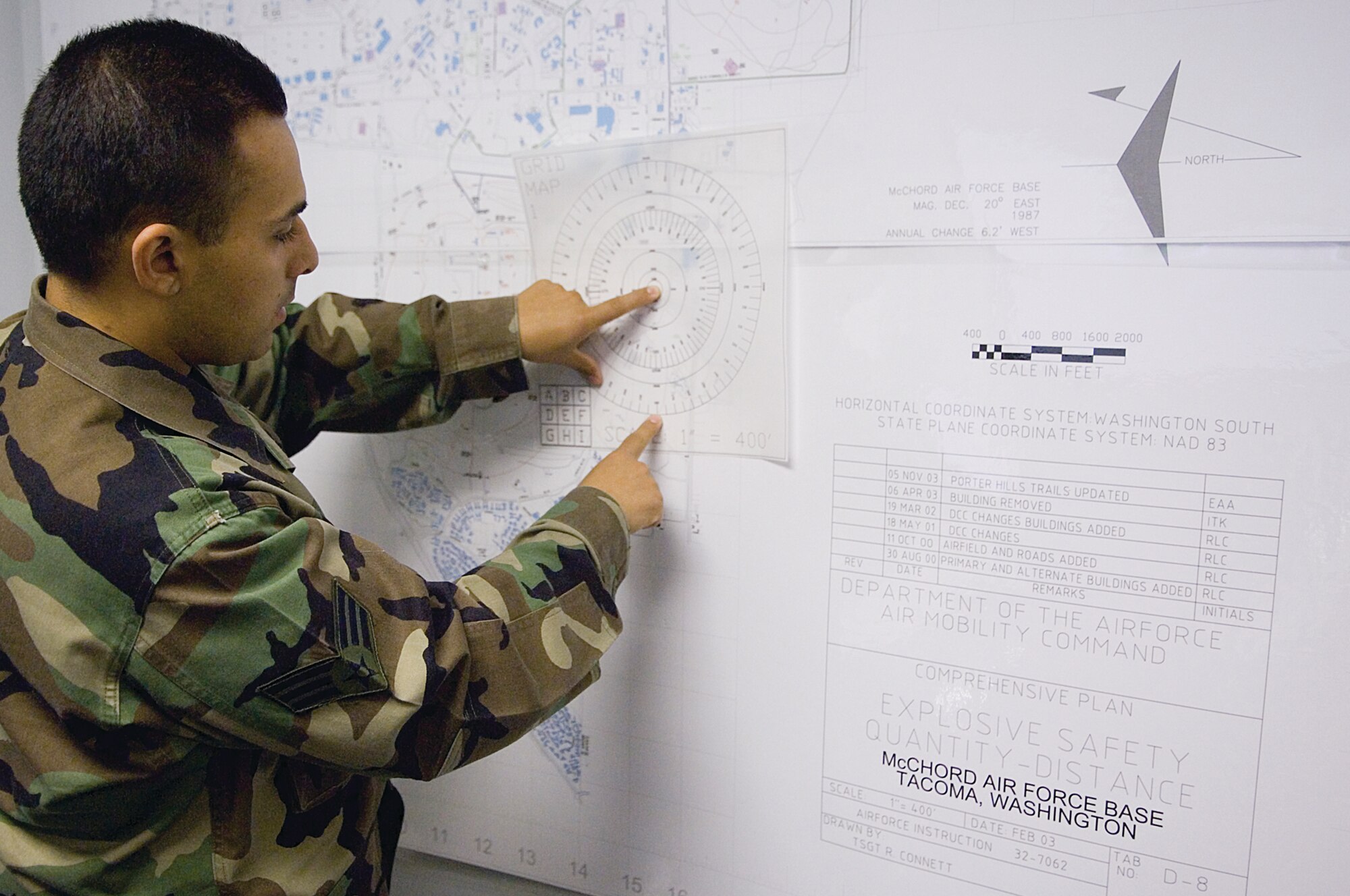 Munitions control center dispatcher Senior Airman Raymond Altamirano, 62nd Maintenance Squadron, uses a grid map placed over a map of McChord to demonstrate the proper procedure used to determine the center's evacuation radius in the event of a real world emergency. As part of a newly proposed plan, the munitions control center would move from its current location south of Outer Drive to a new building north of Whispering Firs Golf Course.