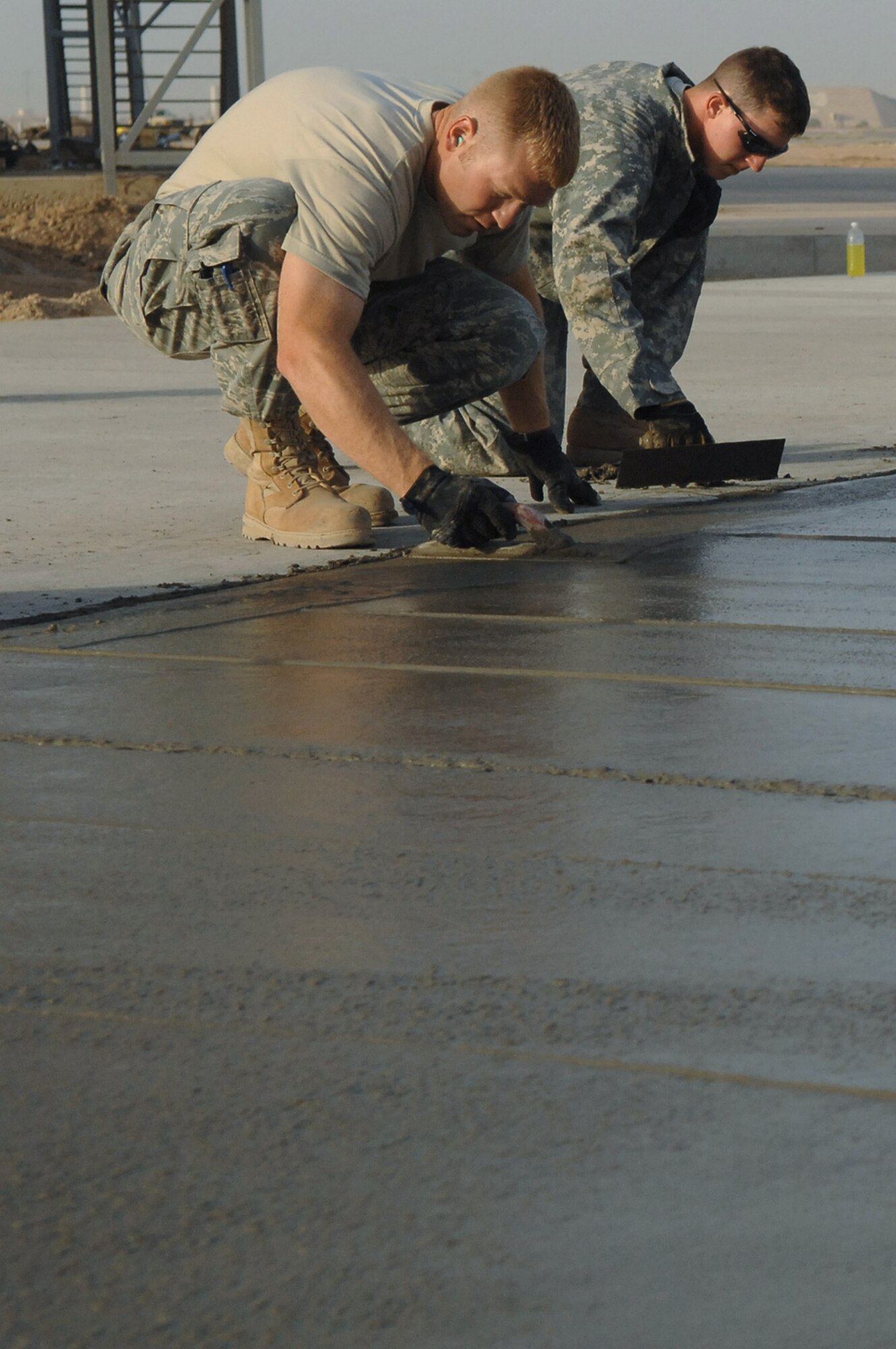 Staff Sgts. Rohde Orlin and Ryan Ward smooth and edge the side of a concrete pad May 13 at Balad Air Base, Iraq. Sergeant Orlin is deployed from Ellsworth Air Force Base, S.D.; and Sergeant Ward is deployed from McConnell AFB, Wash. Both are 332nd Expeditionary Civil Engineer Squadron heavy equipment operators. (U.S. Air Force photo/Senior Airman Julianne Showalter) 