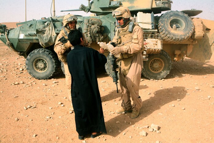 Sgt. Carl J. Woods, 24, a scout squad leader from Virginia Beach, Va., with Delta Company, 2nd Light Armored Reconnaissance Battalion, Regimental Combat Team 5, hands an Iraqi farmer bottles of water while Cpl. Joseph R. Fratti, 22, a scout team leader from Philadelphia, with Delta Company, looks on during a patrol through the western Al Anbar province, Iraq, May 18. The two Marines, along with the rest of the company, patrol through the area, ensuring the civilians are receiving the funding to keep their livestock, sheep and accessories stocked and fed so that they may continue to sustain themselves while also benefiting the future of Iraq.