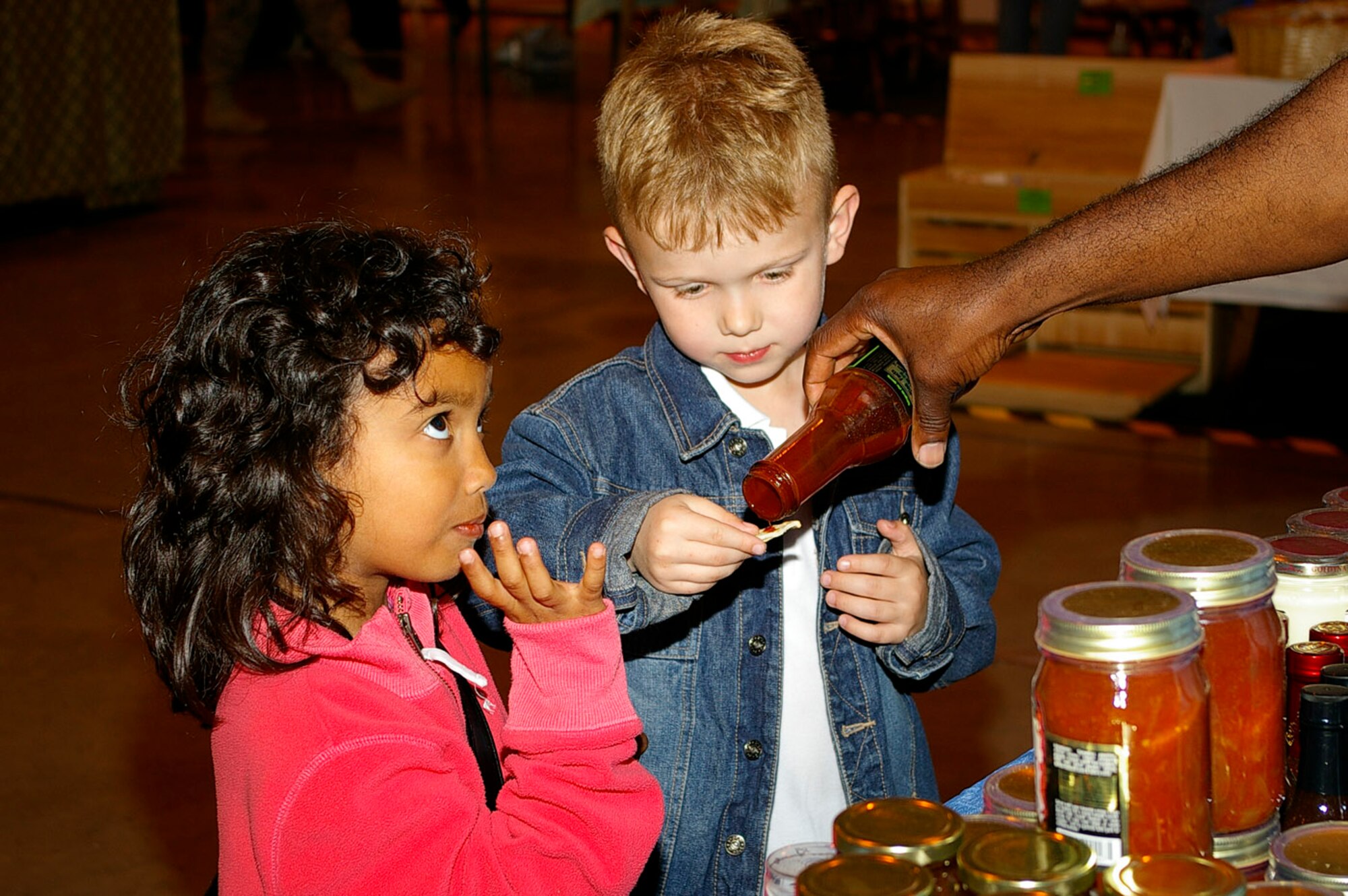 Rebecca Abeyasekere, left, 7, and Jakob Madura, 6, sample some sauces and condiments at the RAF Mildenhall Mayfair Bazaar May 15. (U.S. Air Force photo by Karen Abeyasekere)