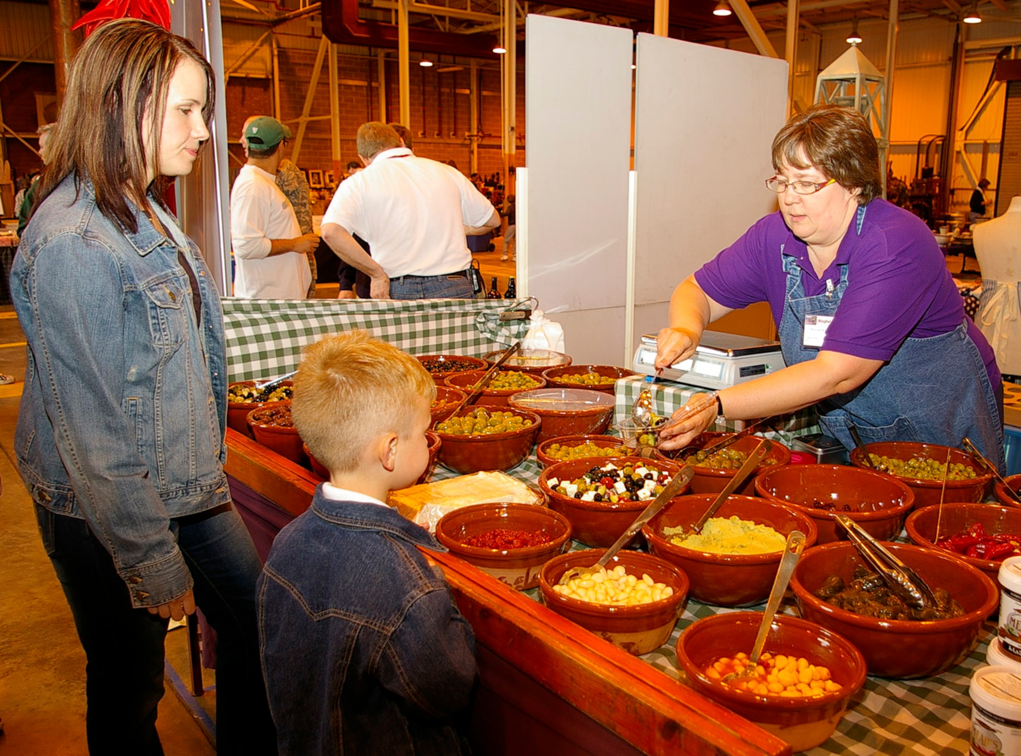 Tech. Sgt. Cathy Madura, left, 100th Air Refueling Wing Judge Advocate Office, and her son Jakob, buy some olives from a vendor at the Mayfair Bazaar May 15. The bazaar is an annual event that attracts vendors from throughout the United Kingdom and Europe. Squadrons from around base had food stands, and the event was free to base ID card holders. The bazaar is one of two bazaars held at RAF Mildenhall. The next bazaar will be the Yuletide Bazaar held at the end of the year. (U.S. Air Force photo by Karen Abeyasekere)
