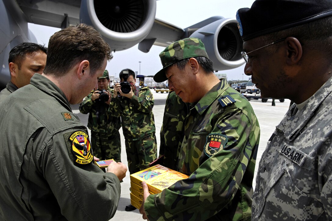 U.S. Air National Guard Maj. Anthony Davis, a C-17 pilot assigned to the 204th Airlift Squadron, presents Senior Capt. Guan Youfei, deputy director of the Chinese Defense Ministry's foreign affairs office, with gifts of traditional Hawaiian chocolates and an American flag patch at Chengdu Shuangliu International Airport in China, May 18, 2008. Davis was the commander of one of the C-17s, which carried nearly 100,000 pounds of relief supplies. Also pictured is Brig. Gen. Charles W. Hooper, U.S. Defense attache. 