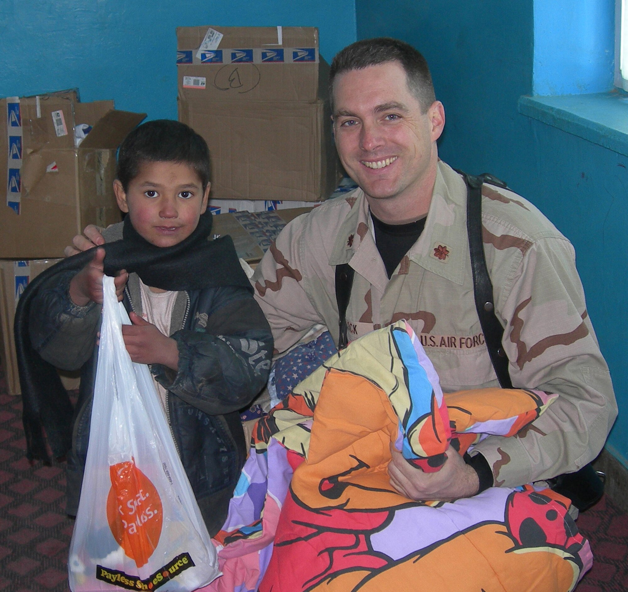 MINOT AIR FORCE BASE, N.D. -- Maj. Jay Block, 91st Maintenance Group chief of quality assurance, poses with an Afghan child at an orphanage in Kabul, Afghanistan, in 2005.  The two are standing in front of boxes of clothing and school supplies donated thanks to Major Block's wife. After hearing the story recently, a group of North Dakota insurance agents and financial planners in Minot raised almost $14,000 in 30 minutes for the orphanage. (Courtesy photo) 