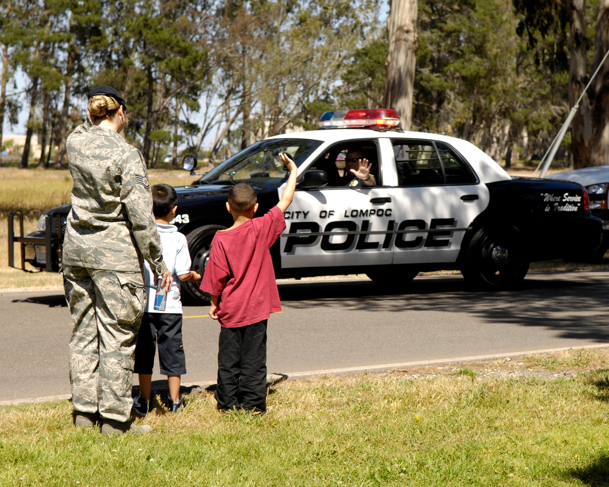 Staff Sgt. Angeline Mason, 30th Security Forces Squadron, her son Devin Mason, and Justin Gilbert wave to a Lompoc Police officer during the Police Week Parade Friday.  The parade ended at Cocheo Park with a BBQ and activities for Vandenberg families.  (U.S. Air Force photo/Airman 1st Class Jonathan Olds)