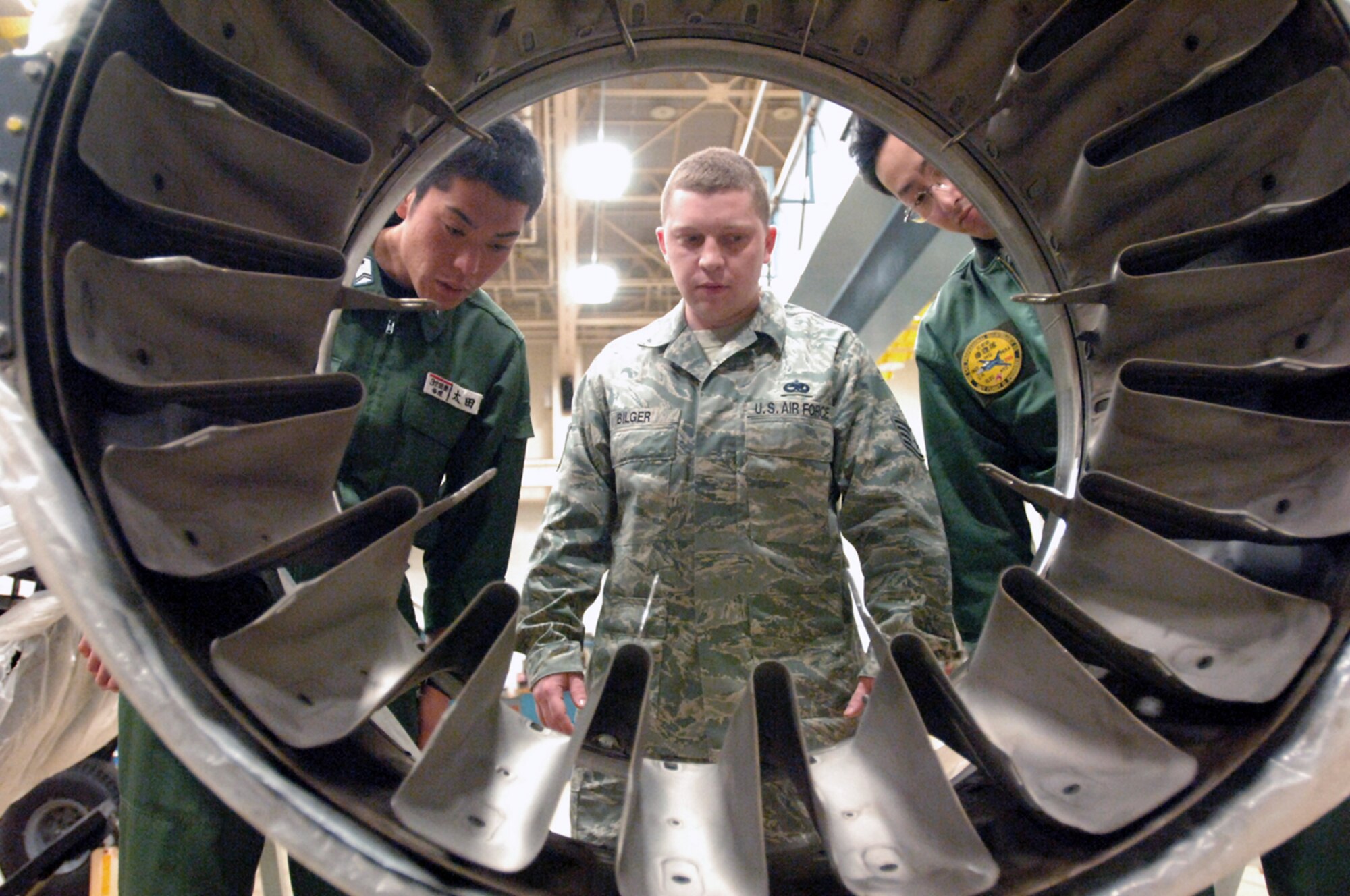 Staff Sgt. Joseph Bilger briefs Japanese Air Self Defense Force Tech. Sgt. Takuma Ota (left) and Staff Sgt. Masanobu Suzuki (right) on the capabilities of an augmentor mixing duct May 15 at Misawa Air Base, Japan. Sergeant Bilger is a 35th propulsion shop jet engine mechanic. (U.S. Air Force photo/Senior Airman Robert Barnett) 
