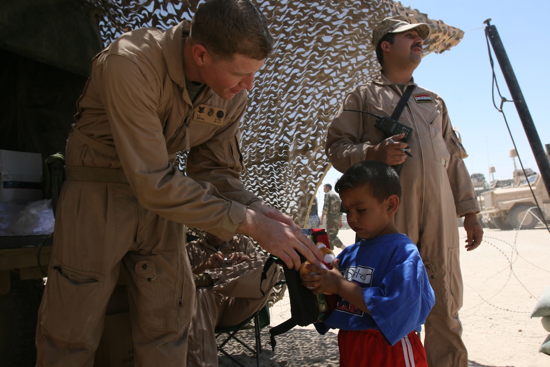 Petty Officer 3rd Class Joshua Moore, religious programmer, 2nd Battalion, 3rd Marine Regiment, Regimental Combat Team 1, hands a teddy bear to an Iraqi girl May 21, in Sitcher, Iraq, during a cooperative medical engagement. More than 1,000 teddy bears were donated from the Oahu Chapter of Zeta Delta Society in Hawaii, to give to the children of Iraq. (Photo by Cpl. Chadwick deBree)