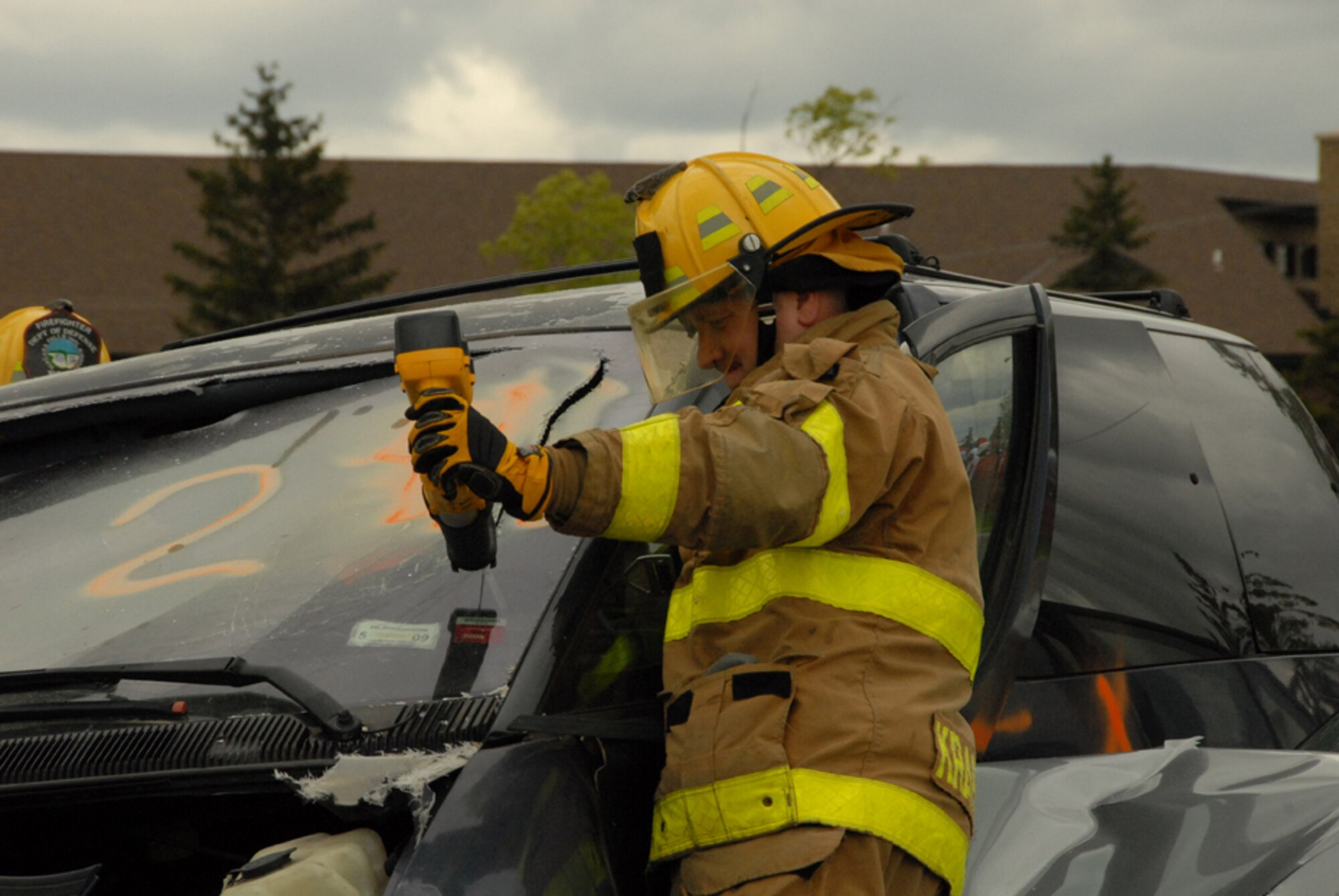 Base firefighter cuts through the front window of a vehicle after crash, as firefighters attempt to remove simulated occupants from the vehicle during the traffic safety program here May 21.  (U.S. Air Force photo/Tech. Sgt. Catherine Perretta).