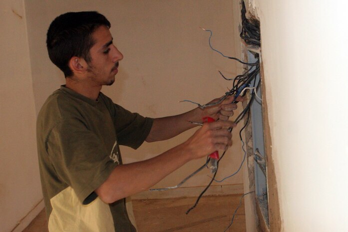 A local worker separates wires to the fuse box at the courthouse in Rawah, Iraq, May 21. The courthouse, which was used by Coalition forces, was demilitarized and is undergoing renovations. The citizens of Rawah were hired by a local contractor to help make repairs before the courthouse was turned over to the city government.