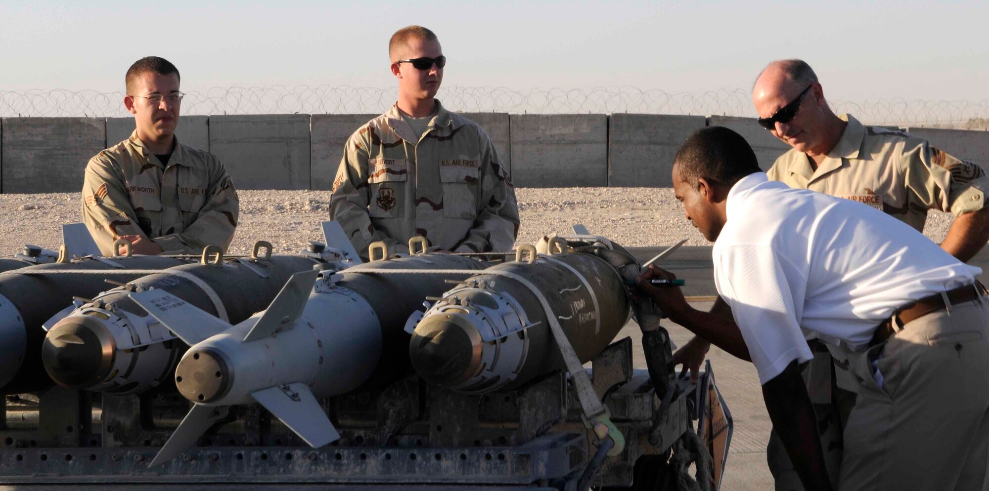 University of Miami head coach Randy Shannon signs a munition with 379th Expeditionary Aircraft Maintenance Squadron specialists Senior Airman Doug Markworth and Staff Sgt. Christopher Seivert during the NCAA coaches tour in Southwest Asia May 22. (U.S. Air Force photo/Tech. Sgt. Johnny Saldivar) 
