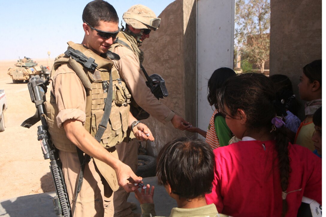 Lance Cpl. Alex C. Brilla, a light armored vehicle crewman, and Lance Cpl. Nathan T. Klink, a scout, both with 1st Platoon, Delta Company, 2nd Light Armored Reconnaissance Battalion, Regimental Combat Team 5, hand out candy to Iraqi children during a support mission for a school in western Al Anbar province, Iraq, May 23. The platoon brought the school wooden benches and seats that Sea Bees had built for the school.