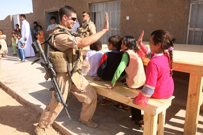 Teaching a part of United States culture, Lance Cpl. Alex C. Brilla, a light armored vehicle operator with 1st Platoon, Delta Company, 2nd Light Armored Reconnaissance Battalion, Regimental Combat Team 5, high-fives a young Iraqi girl during a school re-supply mission May 23 in western Al Anbar province, Iraq. The platoon has been supplying the school for more than a month with school supplies and visiting it as much as they can. When the Marines noticed the students were in need of tables and benches, they sprung into action.