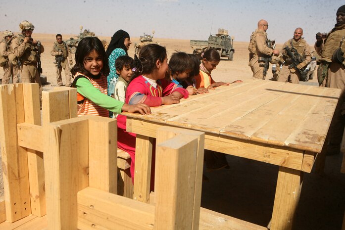 A group of Iraqi children embrace their newly built tables brought to them by 1st Platoon, Delta Company, 2nd Light Armored Reconnaissance Battalion, Regimental Combat Team 5, during a support mission for a school in western Al Anbar province, Iraq, May 23. The Marines delivered the tables to the school and were greeted with a warm embrace from the children and supervisors upon arrival. One by one the children came out to play, sitting on the new benches with smiling faces. According to the Marines with 1st Platoon, seeing the kids' reactions was the greatest part.