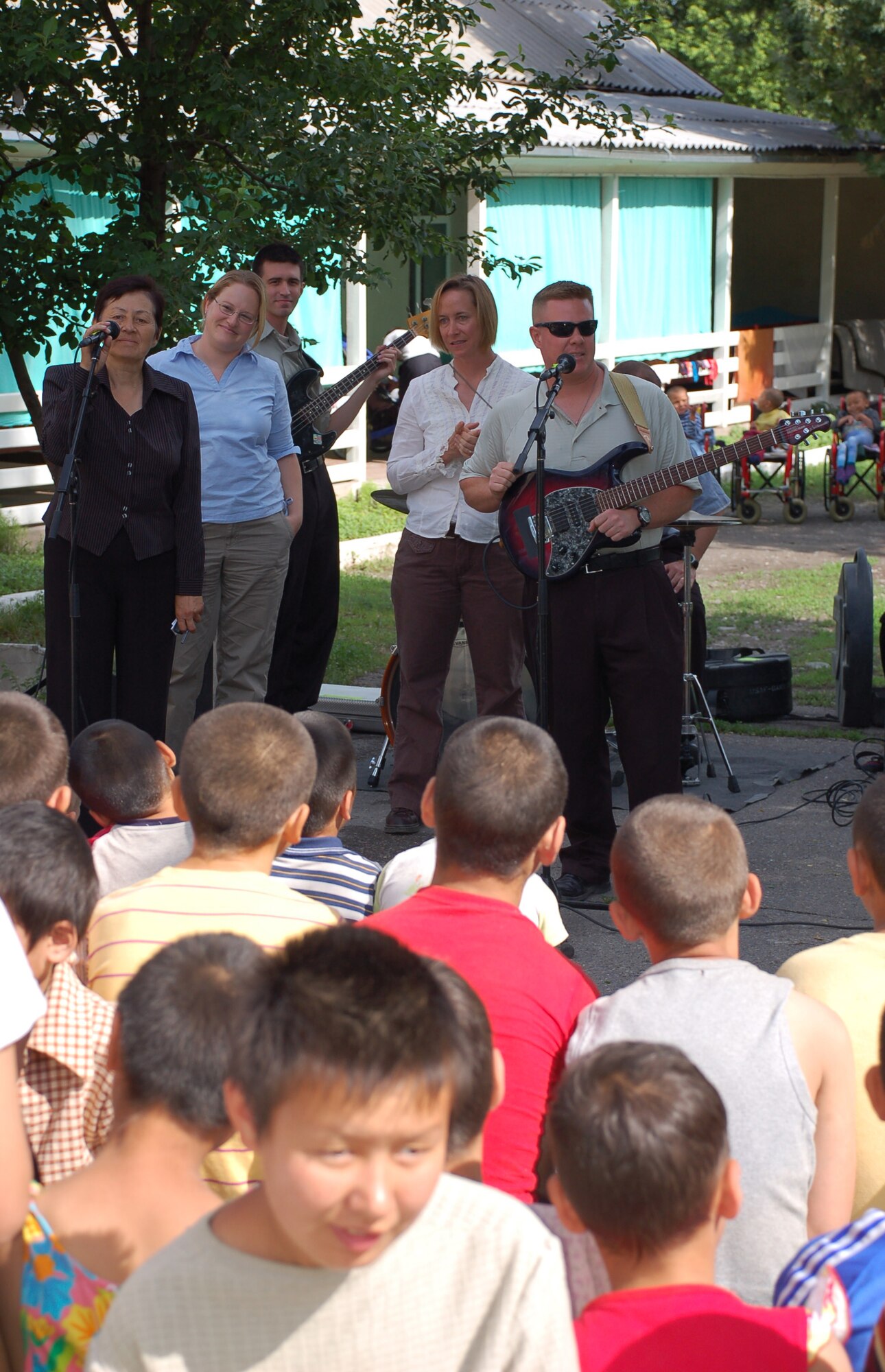 (08/05/25) MANAS AB, KYRGYZSTAN – Ms. Valentina Turabekova, 376th Air Expeditionary Wing interpreter, and Tech. Sgt. Steve Wilson, U.S. Air Forces Central Band Thunder Roll guitarist, introduce themselves to Belovodosky Orphanage children.  The AFCENT band performed at the orphanage and explained the different instruments the band uses during their visit.  (U.S. Air Force/TSgt Jerome Baysmore/ Released)