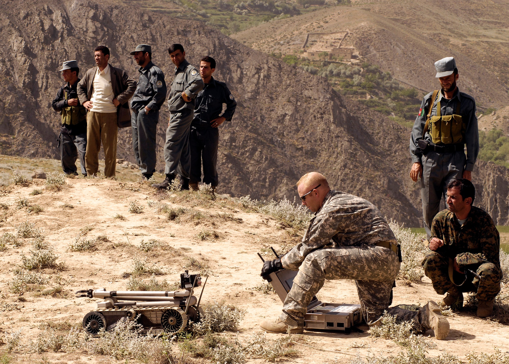 Staff Sgt. Jason Snow prepares to send a PACBOT to an incident site while local authorities look on. A local farmer contacted authorities when he found two 107mm rockets on a timer that were aimed at a coalition forward operating base. Sergeant Snow is deployed as an 755th Air Expeditionary Group robot operator. (U.S. Air Force photo/Master Sgt. Demetrius Lester) 