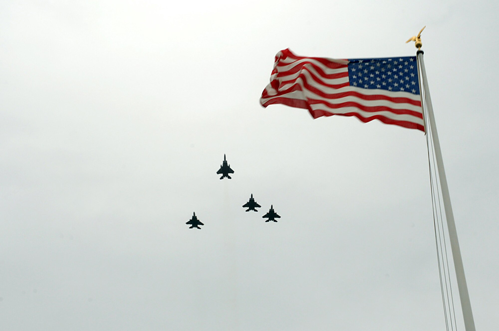 Four F-15C's from RAF Lakenheath perform the missing man formation during the memorial ceremony at Madingly May 26. Pilots fly this solemn aerial maneuver as a tribute and showing of love, respect, and camaraderie for fellow servicemembers who have been lost fighting for freedom. (U.S. Air Force photo by Airman 1st Class John Easterling)