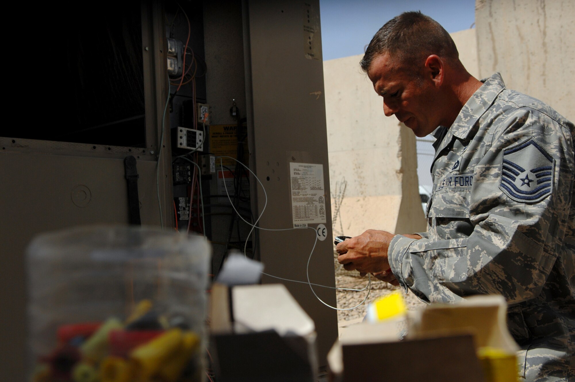 BALAD AIR BASE, Iraq -- Master Sgt. Jason Dean, 332nd Expeditionary Civil Engineer Squadron heating, ventilation and air conditioning special project manager, strips the plastic casing off of copper cable used in a packaged air conditioning system here, May 26. The system is used to maintain cool temperatures surrounding mission essential computer equipment in the Air Terminal Operations Center. Most daily temperatures at Balad AB this month have been either at or above 100 degrees Fahrenheit. Sergeant Dean is deployed from F.E. Warren Air Force Base, Wyo. (U.S. Air Force photo/ Senior Airman Julianne Showalter)