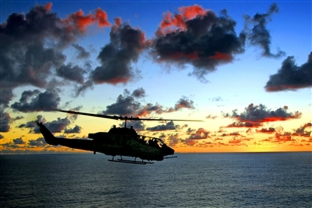 A Marine AH-1A Super Cobra fast-attack helicopter passes by the amphibious assault ship USS Tarawa during sunset over the Pacific Ocean, May 21, 2008. The USS Tarawa is on a scheduled deployment to the U.S. 7th Fleet area of responsibility operating in the western Pacific and Indian oceans. 