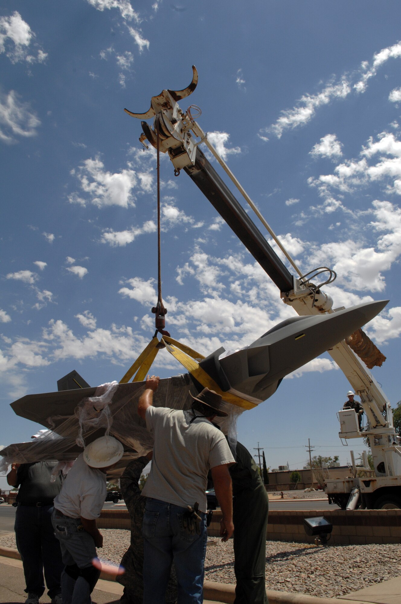 Members of Team Holloman help support the model of an F-22A Raptor while it?s hoisted in the air in front of the 49th Fighter Wing headquarters building at Holloman Air Force Base, N.M., May 20. The crane was used to move the 375-pound model from the carrier it was delivered on to the stand on which it will be displayed. The model is one-fifth the size of an actual Raptor. (U.S. Air Force photo/Airman Sondra M. Wieseler)
