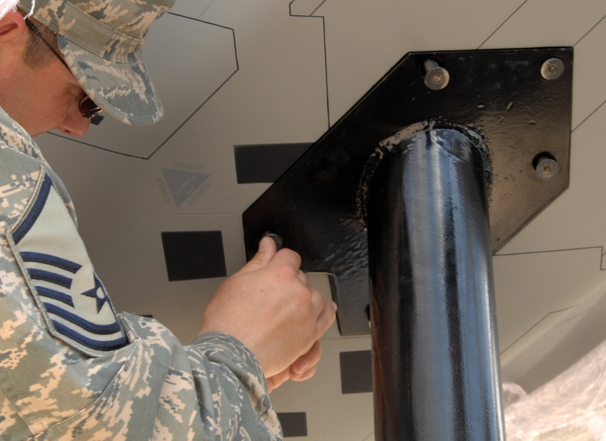 Master Sgt. John Profitt, 49th Civil Engineer Squadron, tightens a bolt underneath the model F-22A Raptor to secure it to it?s stand at the 49th Fighter Wing headquarters building at Holloman Air Force Base, N.M., May 20. The model took the place of the model F-117A Nighthawk and now sits in front of the building along with the model of a German Tornado. The model Raptor is 13-feet in length and has a 9-foot wingspan, one-fifth the size of the actual aircraft. (U.S. Air Force photo/Airman Sondra M. Wieseler)