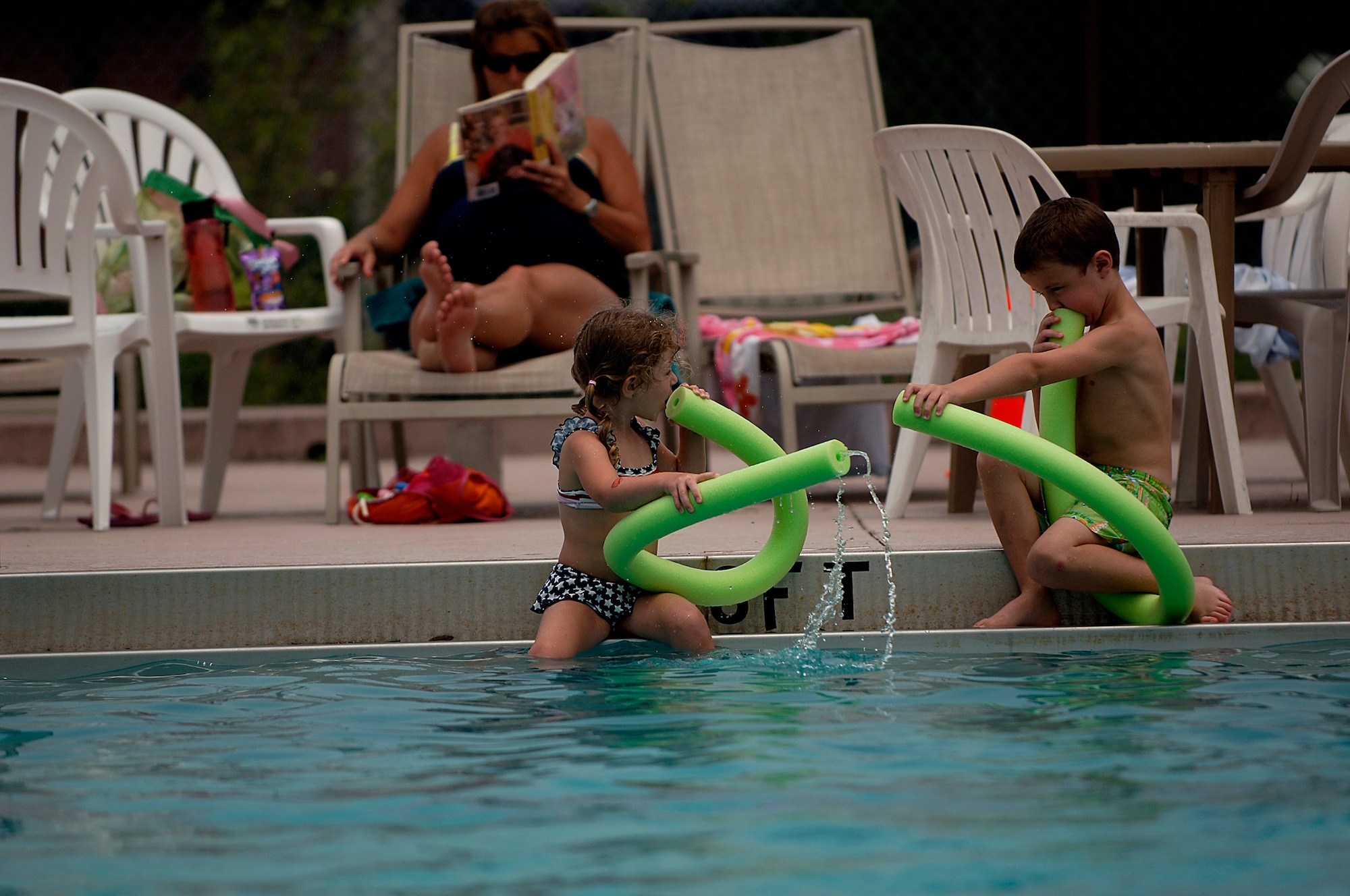 Gabe and Paige Davenport play in the water while their mother, Leann Davenport reads a book at the base pool May 24. Gabe, 5, and Paige, 4, are the children of Steven and Leann Davenport. (U.S. Air Force photo/Senior Airman Nicholas Pilch)