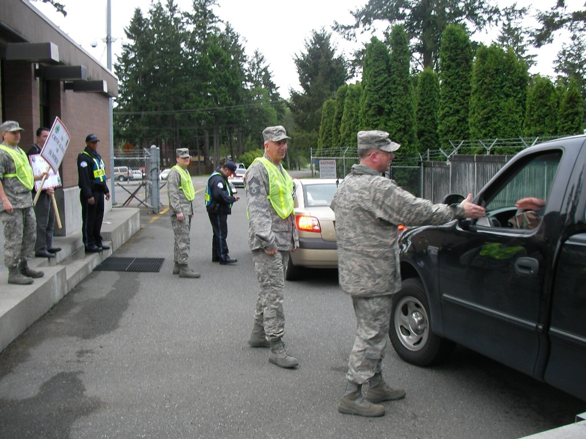 Col. Frank Rechner, 62nd Mission Support Group commander, right, and Chief Master Sgt. Cary Hatzinger, 62nd MSG superintendent, center, greet drivers at the family housing gate May 22. It is a tradition for leadership to remind members of Team McChord to be safe prior to long weekends. (U.S. Air Force photo/Staff Sgt. Eric Burks)