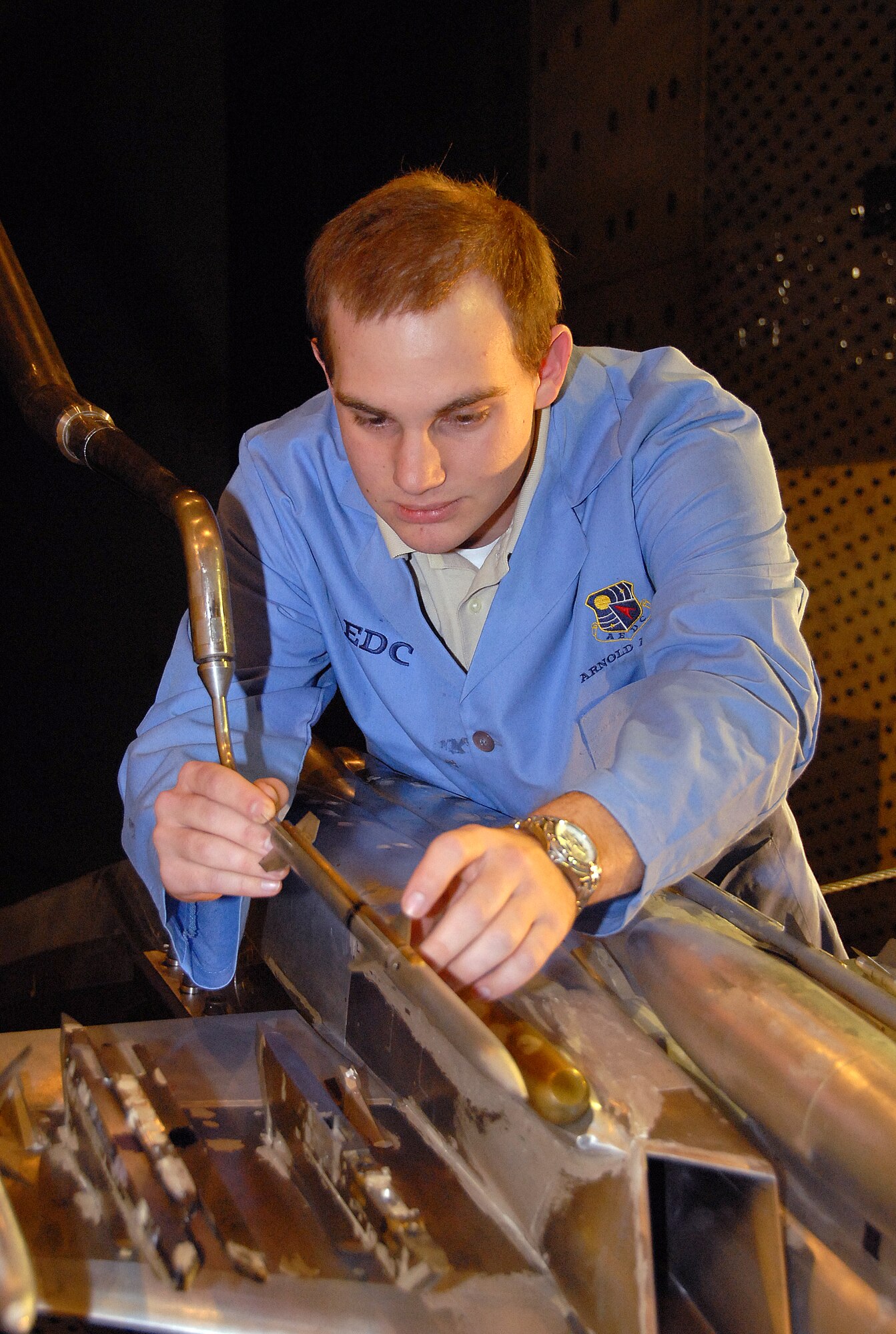 Adam Burt, a co-op student working with Aerospace Testing Alliance, inspects the 1/10-scale models of the sting-mounted AIM-120C store and F/A-18E/F aircraft during a break in store separation testing inside AEDC’s 16-foot transonic wind tunnel. ATA is the support contractor for the center. The ongoing testing marks the 13th entry of the Super Hornet for store separation testing in 16T. The data from the testing goes into a database and leads to flight testing. (Photo by David Housch)