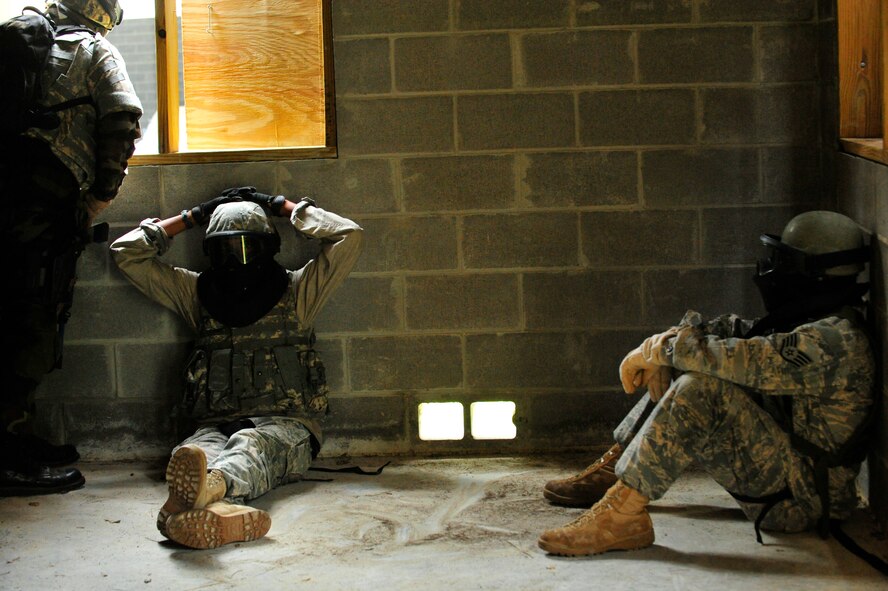 MOODY AIR FORCE BASE, Ga -- Two simulated enemy prisoners of war sit under guard as Senior Master Sgt. Ron Hall, 820th Security Forces Group operations analysis superintendent, calls out to his team leader that the building has been secured during combat medical skills training here May 22. Airmen use real-world tactics when training to ensure they are able to handle real world combat stresses. Sergeant Hall is currently deployed in Iraq and is using the skills he learned from the pre-deployment training. (U.S. Air Force photo by Senior Airman Schelli Jones) 
