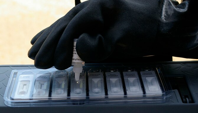 Senior Airman Neal Clark puts droplets of a sample from the outside of the suspicious package onto a tray of chemical agent detectors. A sample of the powder was taken, put into a small bottle then mixed with a special liquid and shaken, before carefully putting small amounts onto the sample tray during the exercise May 23. (U.S. Air Force photo taken by Karen Abeyasekere)