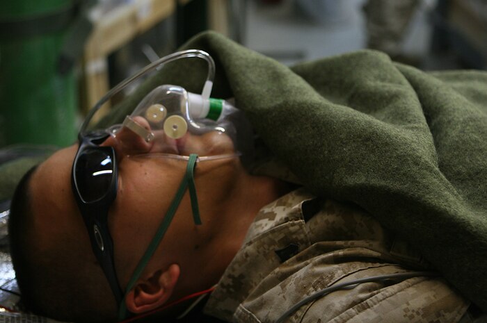 Cpl. Edward Gentry, a radio technician with Communications Platoon, Headquarters and Service Company, Task Force 2nd Battalion, 2nd Marines, Regimental Combat Team 5, lies motionless on a litter with an oxygen mask as he plays the role of simulated casualty at Camp Korean Village, Iraq, May 30. Gentry was one of many simulated casualties who participated in a mass casualty drill to test the Marines and sailors response time in the event of an attack resulting in injuries.
