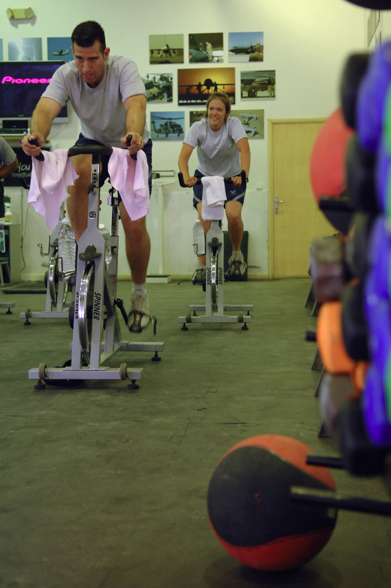 BALAD AIR BASE, Iraq -- Tech. Sgt. Emmanuel Ramirez, 332nd Expeditionary Civil Engineer Squadron power production technician, and Staff Sgt. Rachel Schultz, 777th Expeditionary Aircraft Maintenance Unit hydraulic specialist, cycle on stationary bikes during a class at the Red Tail Fitness Center here, May 31. Besides being a great form of aerobic activity, indoor cycling is also beneficial in strengthening the muscles of the lower body. It tones the quadriceps and hamstrings, along with working the back and hips. Maintaining a healthy, physically fit lifestyle helps Airmen to carry out their daily duties more efficiently in a deployed environment. Sergeant Ramirez is deployed from Peterson Air Force Base, Colo., and Sergeant Schultz is deployed from Little Rock Air Force Base, Ark. (U.S. Air Force photo/ Senior Airman Julianne Showalter)