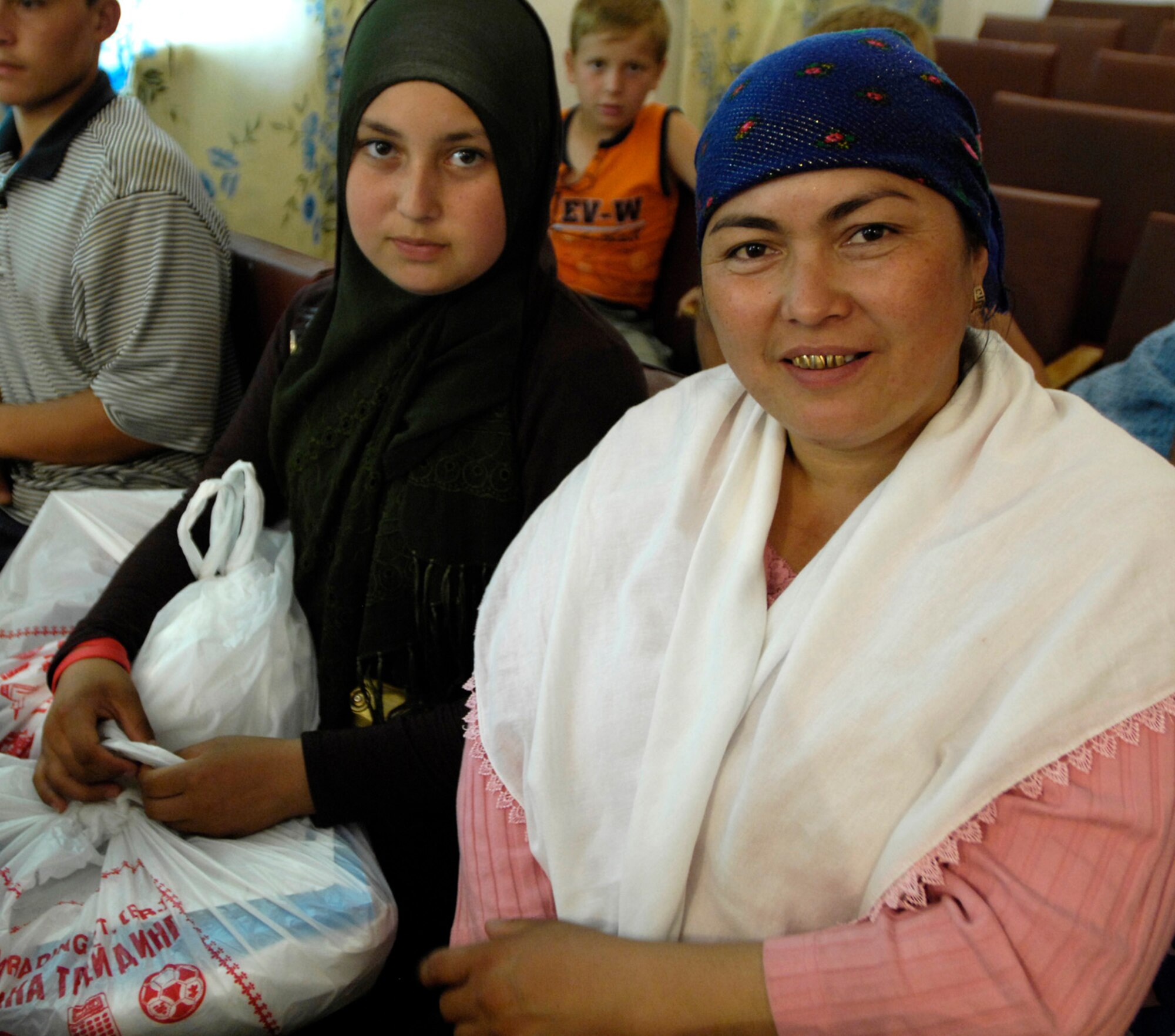 Less fortunate members of Oktyabrskoye village watch as their children receive gift bags from Airmen of the 376th Expeditionary Security Forces Squadron, Manas Air Base, Kyrgyz Republic, on May 30 as part of the village's recognition of International Protection Day, which is June 1. The Airmen delivered gift bags of hygiene products, T-shirts,  towels, candy, coloring books, toys, and other much needed supplies. The items were purchased with money allocated from the private organizations on base and with donations from home units of the security forces members. (U.S. Air Force Photo by Staff Sgt. Tabitha Kuykendall) (RELEASED) 