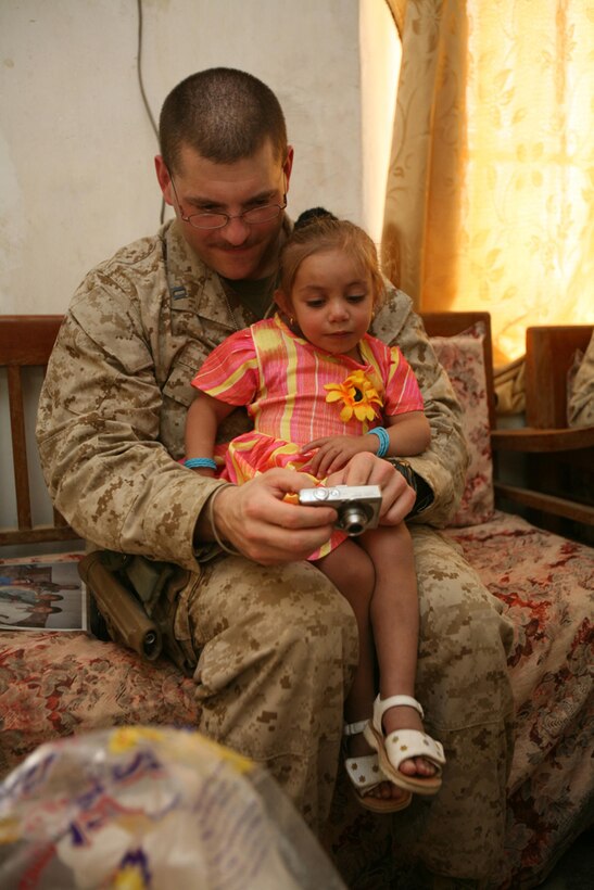 Navy Lt. Benjamin D. Wind, the battalion surgeon with 3rd Battalion, 4th Marine Regiment, Regimental Combat Team, shows his photos to Amenah Al'a Thabit at her home in Haditha, Iraq, June 20. Marines with the battalion escorted Wind to check on how Amenah was doing after having surgery in January at Vanderbilt University in Nashville, Tenn., to correct a congenital heart condition. The success of Amenah's case opened the doors for more children in the area to receive medical treatment with the help of Coalition forces and the local Iraqi government. Since her case, two more children have traveled out of Iraq to have surgery for the same condition.::r::::n::