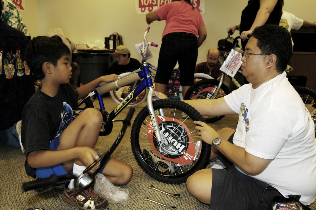 Daniel Yu-Cua and BAE Systems employee Alan Isobe, assemble one of more than 100 bicycles donated by the company's employees to the Marine Corps' Toys for Tots program. BAE Systems' 'Bikes for Tykes' event is in its third year, and more than 65 employees turned out Saturday morning to assemble the bikes.