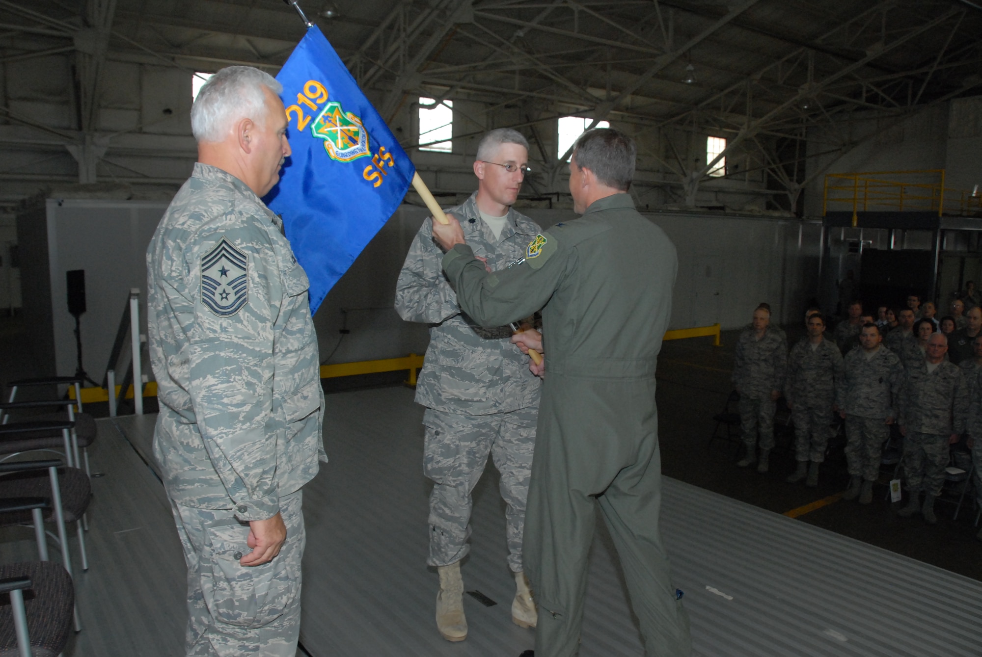 Col. Robert Becklund, 119th Wing Commander, hands the 219th Security Forces Squadron flag to Lt.Col. Tad Schauer, 219th SFS Commander, as CMSgt Bradley Childs, 119th Wing Command Chief stands at attention during an activation ceremony for the new squadron conducted at Minot Air Force Base in N.D. on Oct. 18.