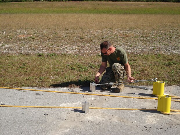 Staff Sgt. James Seeger, 2nd Marine Aircraft Wing, Marine Corps Air Station New River, N.C., adjusts a turnbuckle connecting two stakes, which is part of an M-31 Marine Corps Expeditionary Arresting Gear System. The system was constructed for the 2nd Annual Space & Air Show at Kennedy Space Center Nov. 9.