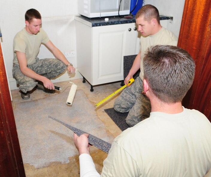 From left to right, Airman Cody Seymour, Airman Scott Ricketts and Staff Sgt. Richard Podry, all 100th Civil Engineer Squadron Structures Shop Airmen, apply glue ready to lay carpet tiles on the floor of the kitchen area in the 100th Air Refueling Wing headquarters building Oct. 29. The structures shop personnel are responsible for maintaining buildings on base and their job includes dealing with roof leaks, replacing doors, and the overall structural integrity of buildings. (U.S. Air Force photo by Karen Abeyasekere)