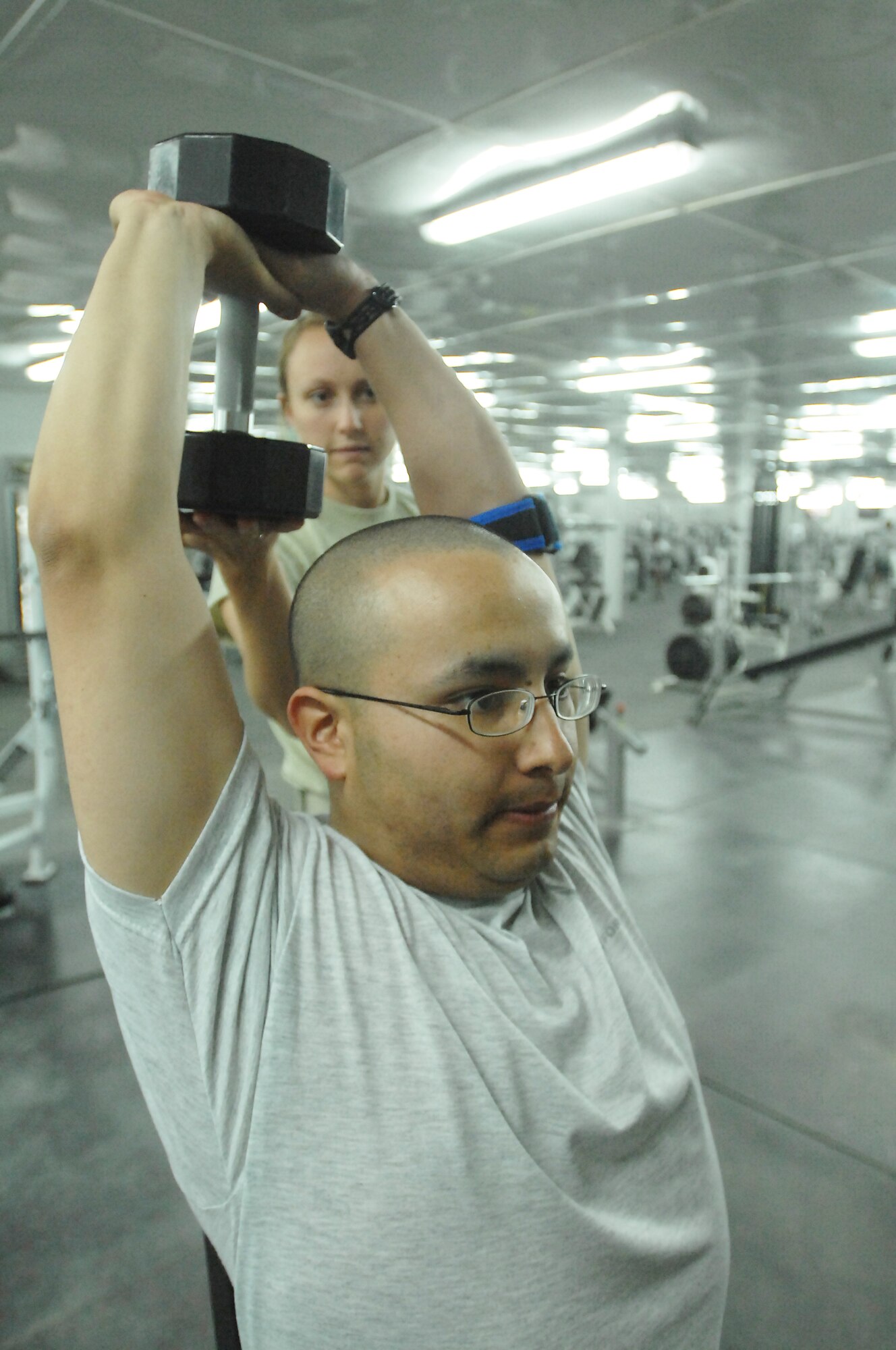 ALI BASE, Iraq -- Performing a seating dumbbell extension, Staff Sgt. Jose Berrios Jr. tackles his first workout session with the guidance of Senior Airman Jessica Mead, 407th Expeditionary Force Support Squadron personal trainer, at the fitness center here Oct. 3, 2008. As a personal trainer, Mead teaches her clients the proper form while using free weights and other equipment. Mead, a Johnson City, N.Y. native, is deployed from Mountain Home Air Force Base, Idaho. Berrios is assigned to the 407th Expeditionary Security Forces Squadron Force Protection and is deployed from the 59th Mental Health Squadron, Lackland AFB, Texas. He is a native of Pearsall, Texas. (U.S. Air Force photo/Tech. Sgt. Francesca Popp)