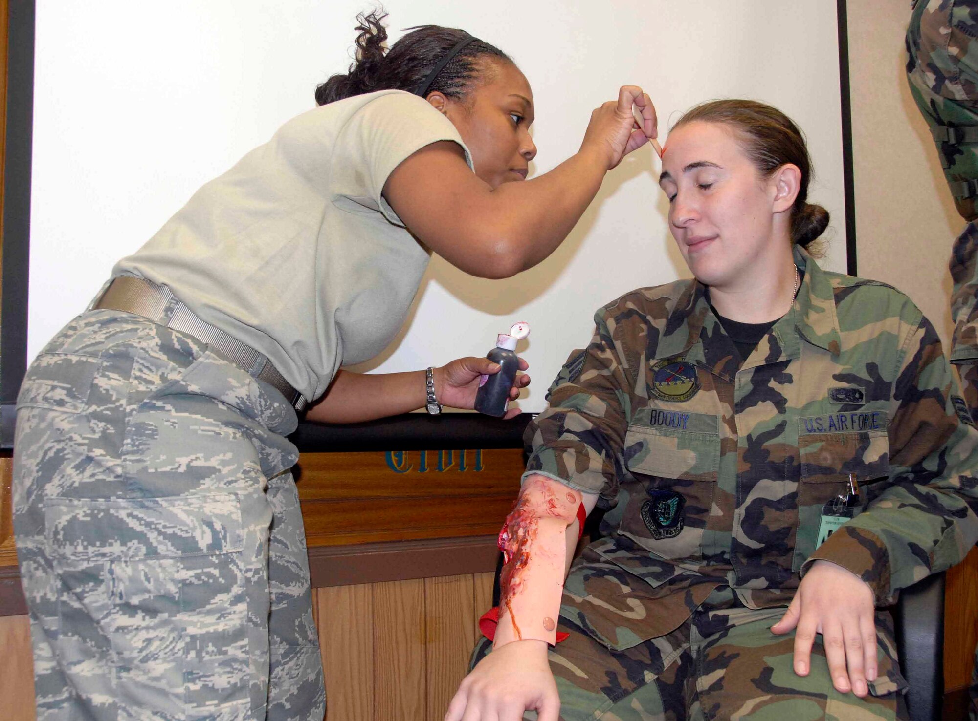 OSAN AIR BASE, Republic of Korea -- (From left to right) Staff Sgt. Aschia Frederick, 51st Medical Support Squadron laboratory technician, applies makeup to Senior Airman Karla Boody, 51st Maintenance Squadron, to enhance Airman Boody's role as a "wounded" citizen in a mass casualty simulation during a base-wide exercise Nov. 3. The exercise tests base personnel's ability to transition from peacetime to wartime operations, execution of the mission in a war time environment, and response time to major accidents and natural disasters. (U.S. Air Force photo/Staff Sgt. Lakisha Croley)