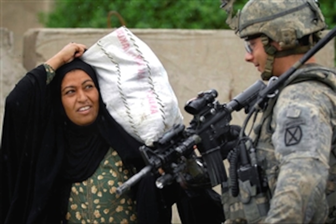 A U.S. Army soldier greets an Iraqi woman carrying a bag in the Doura community of southern Baghdad, Iraq, Oct. 29, 2008. The soldier is assigned to the 4th Infantry Division's 2nd Battalion, 4th Infantry Regiment.